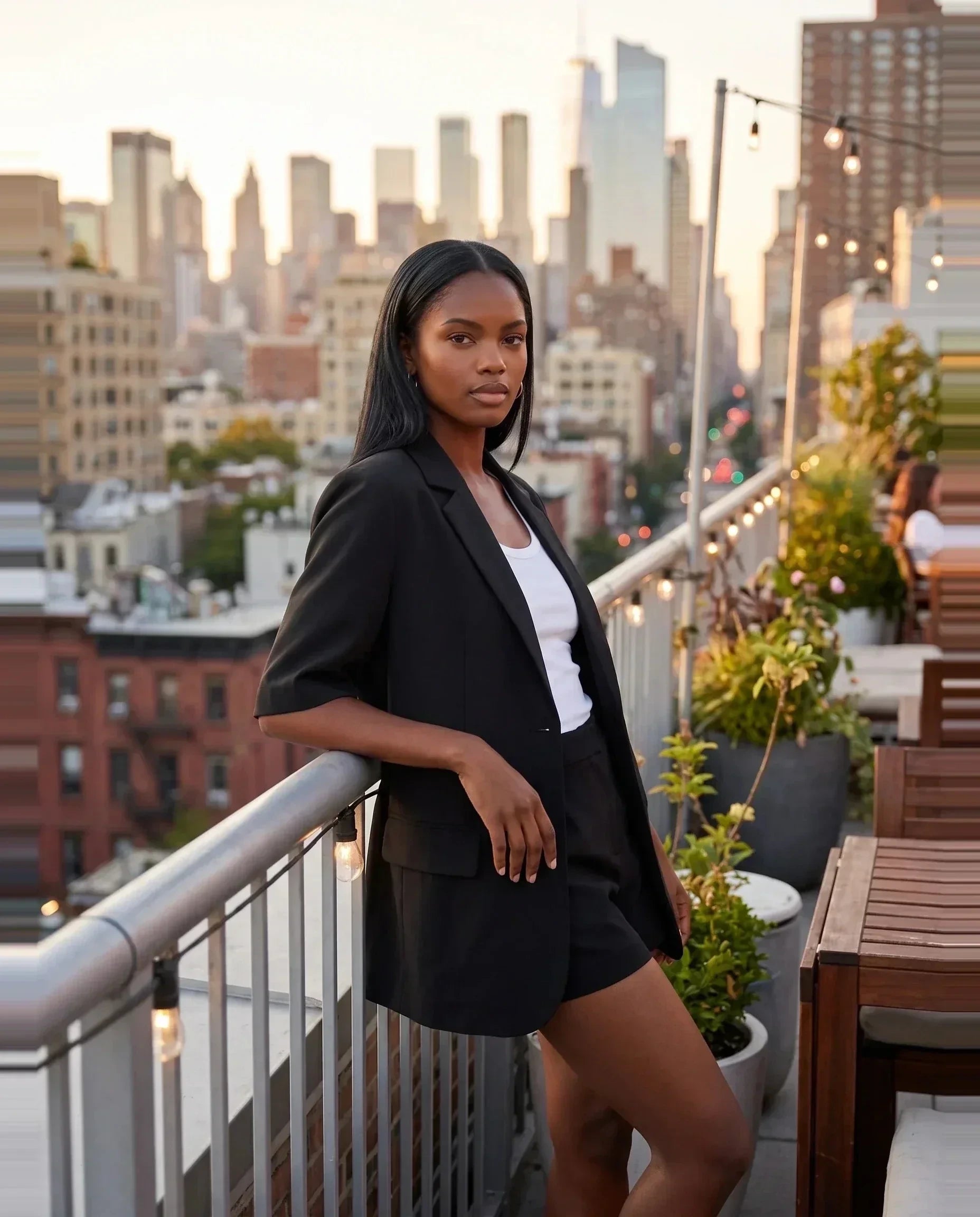 Blazer manches courtes noir Arlette, porté sur un rooftop à l'heure dorée