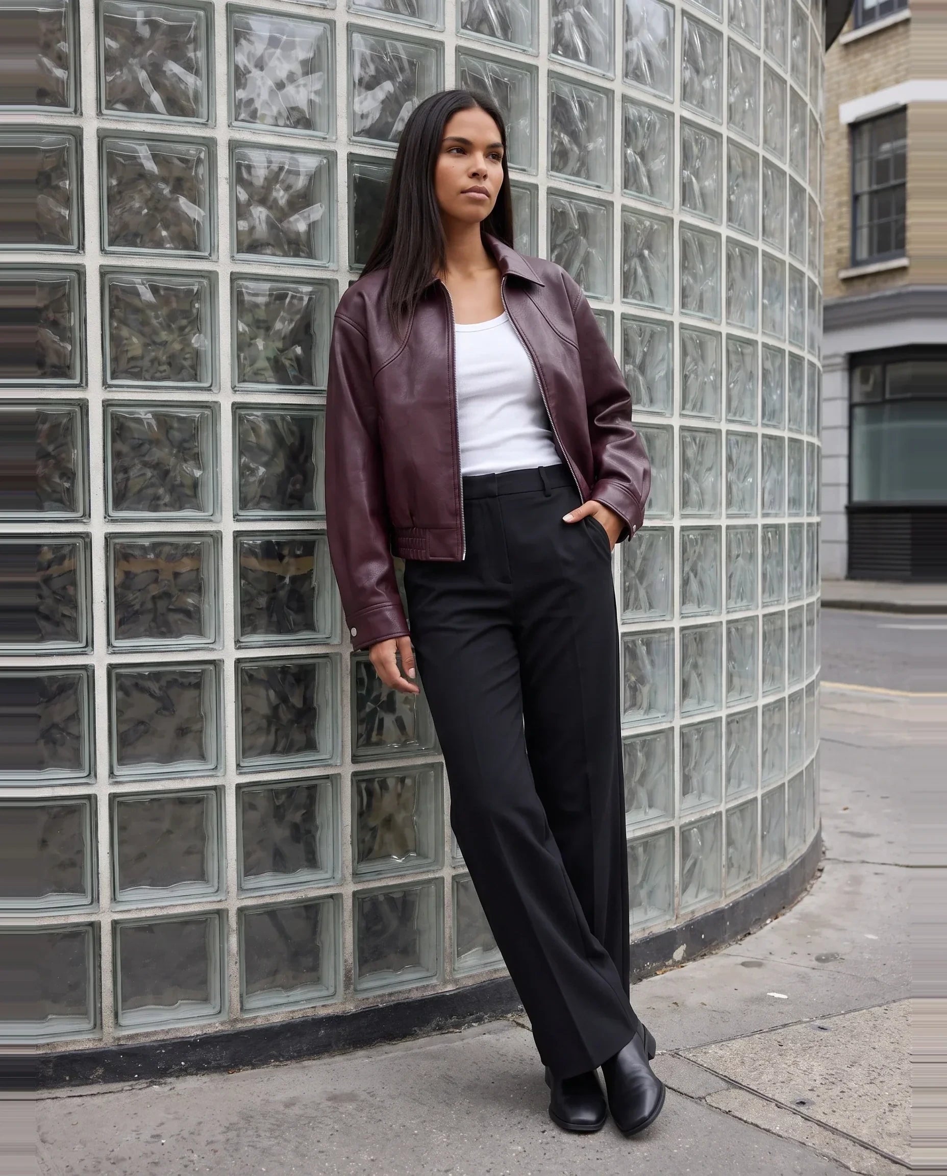 Blouson moto effet cuir lie de vin Marcelle, porté devant un mur de briques de verre