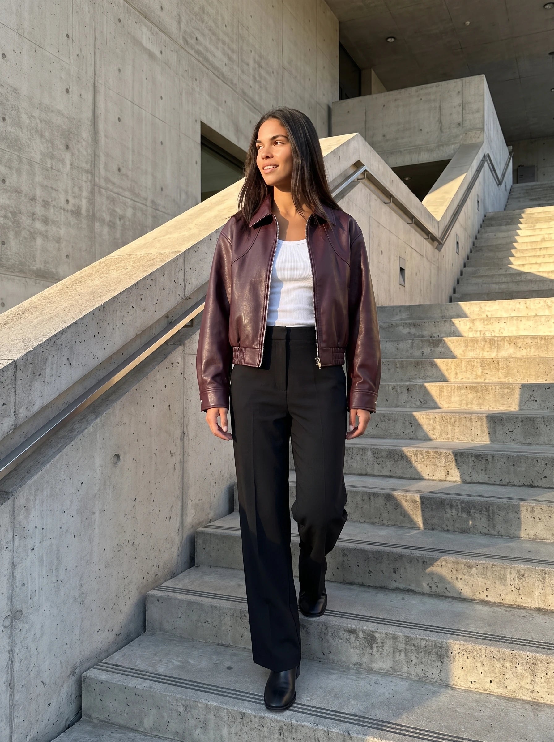 Blouson moto effet cuir lie de vin Marcelle, porté dans un escalier de musée en béton