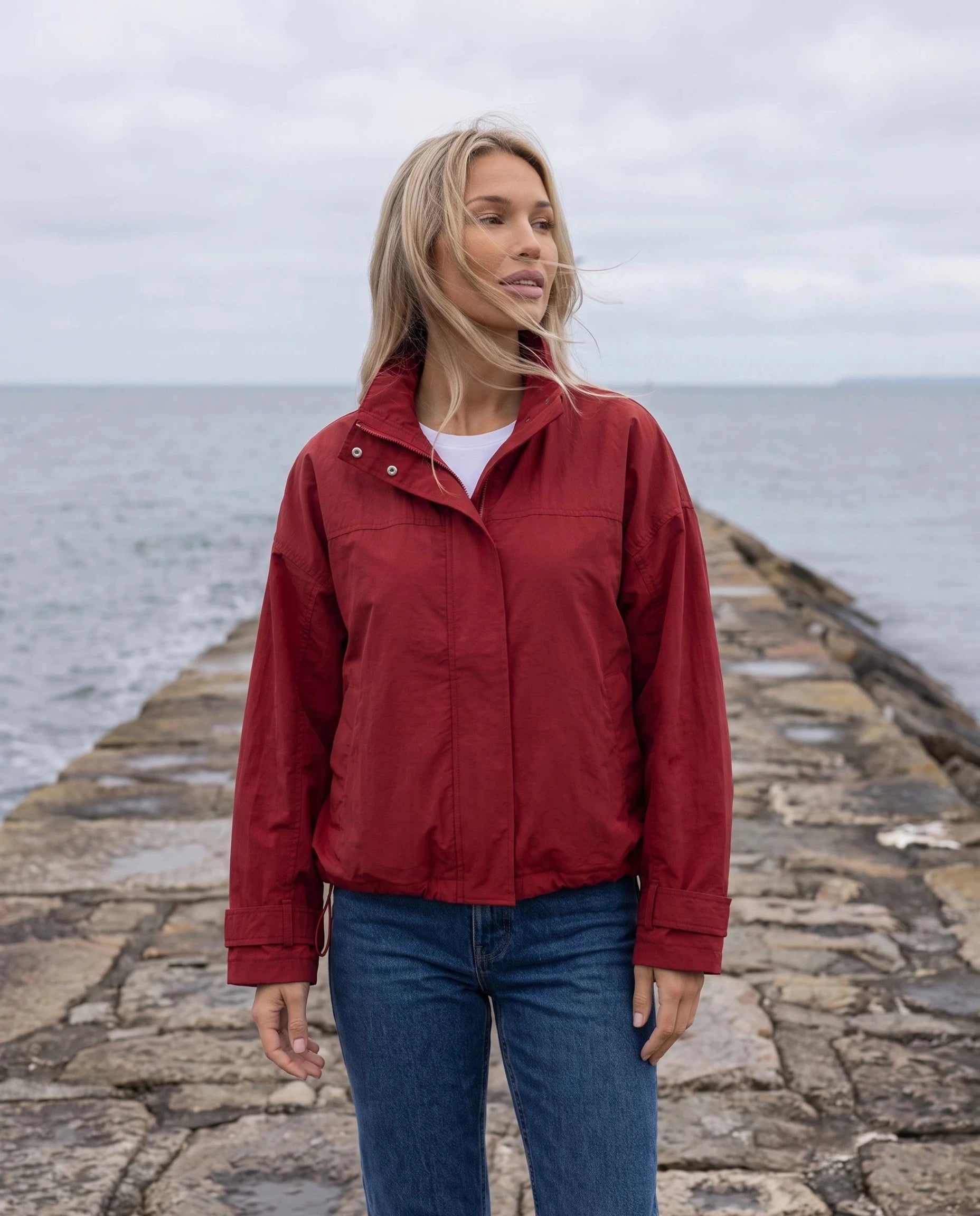 Coupe-vent rouge Ursule, porté sur une jetée de pierre face à la mer