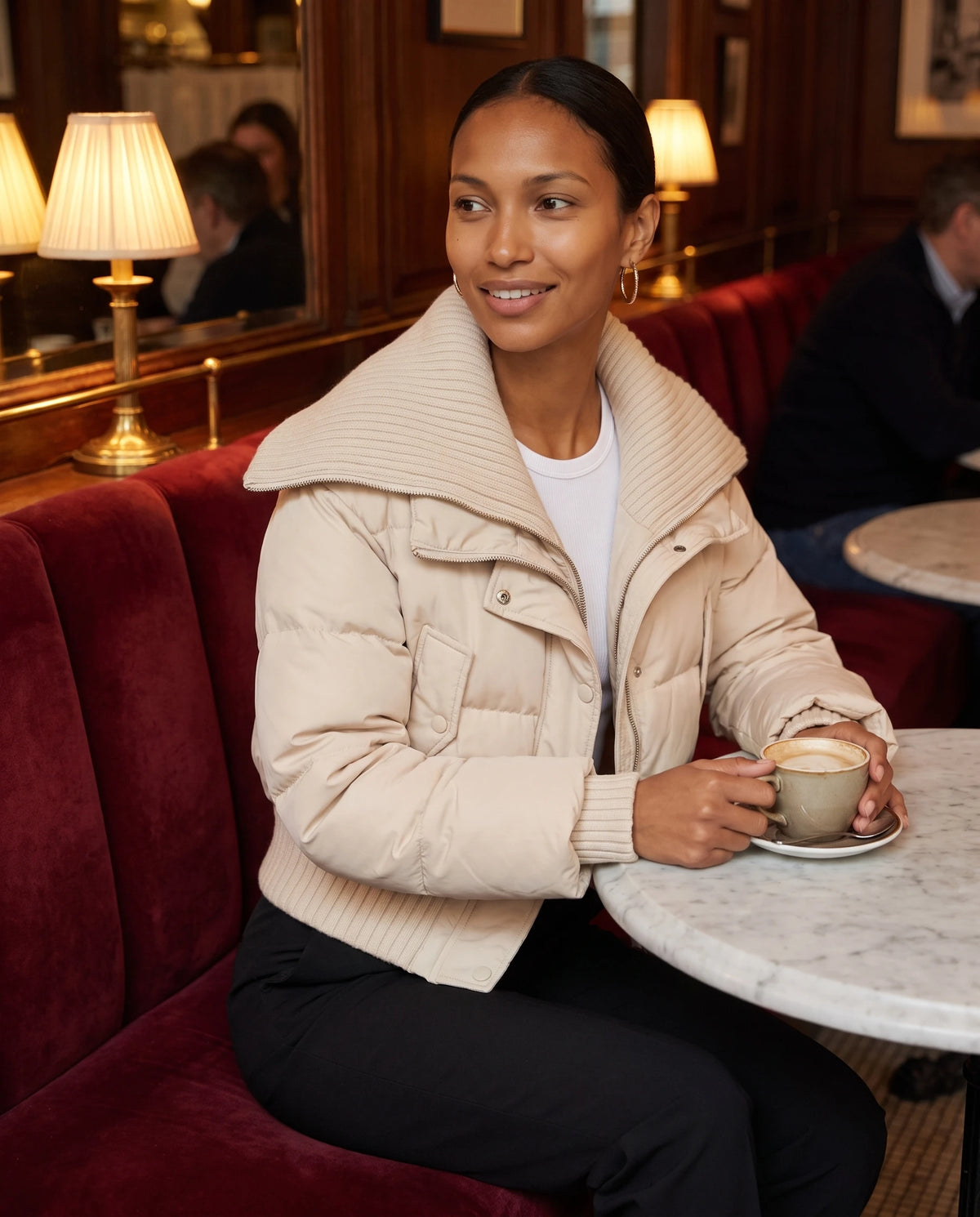 Doudoune courte à col tricot Nella en Beige, portée dans un café aux banquettes en velours