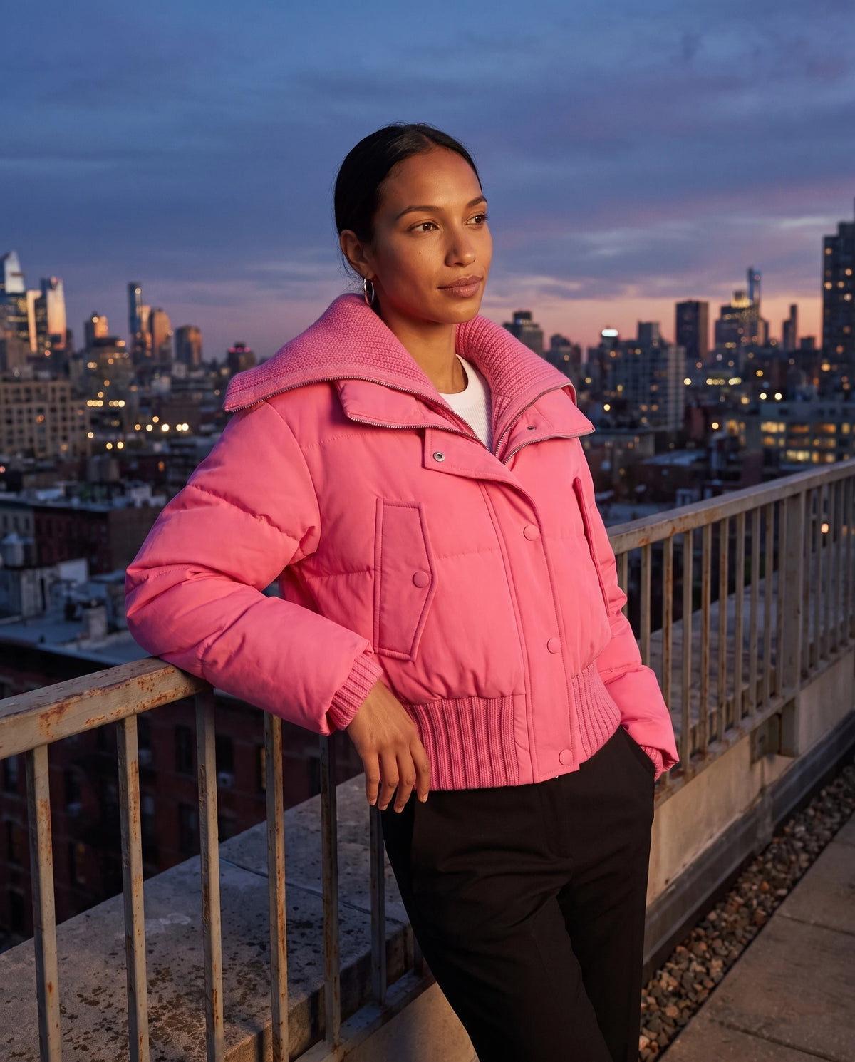 Doudoune courte à col tricot Nella en Rose Vif, portée sur un rooftop au crépuscule