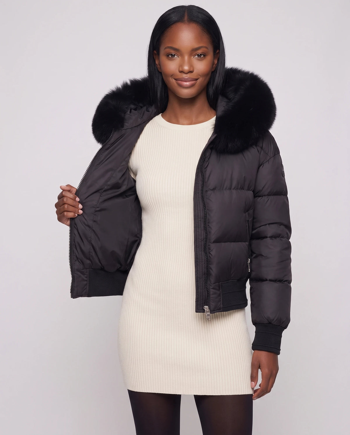 Kurze Steppjacke mit grosser Kunstfellkapuze Rebecca in Schwarz · schwarzes Fell, offen getragen über cremefarbenem Strickkleid