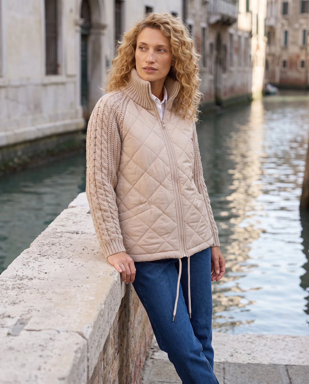 Doudoune courte à manches tricot Emma en Beige, portée sur un quai de canal en pierre claire