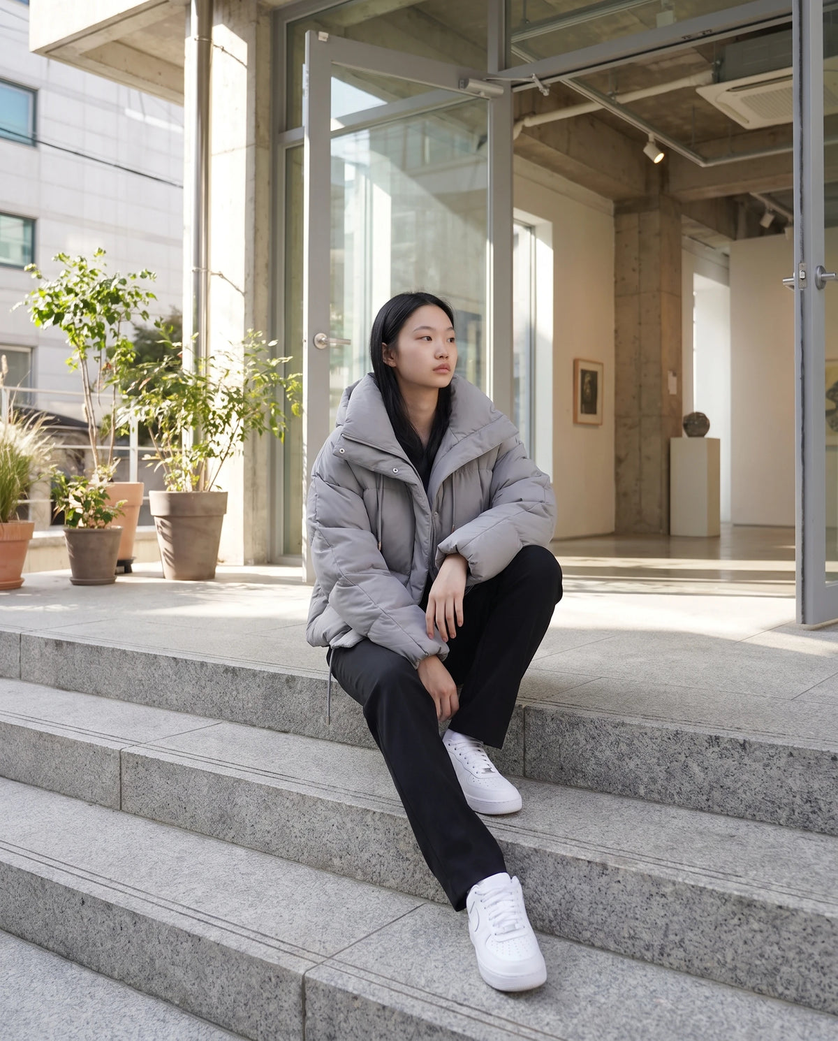 Cropped Pufferjacke Sabelline in Grau, getragen auf den Stufen einer Galerie