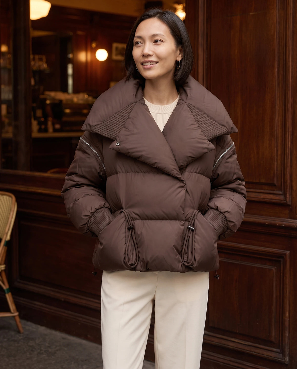 Doudoune courte à grand col matelassé Katell en Chocolat, portée devant un café aux boiseries