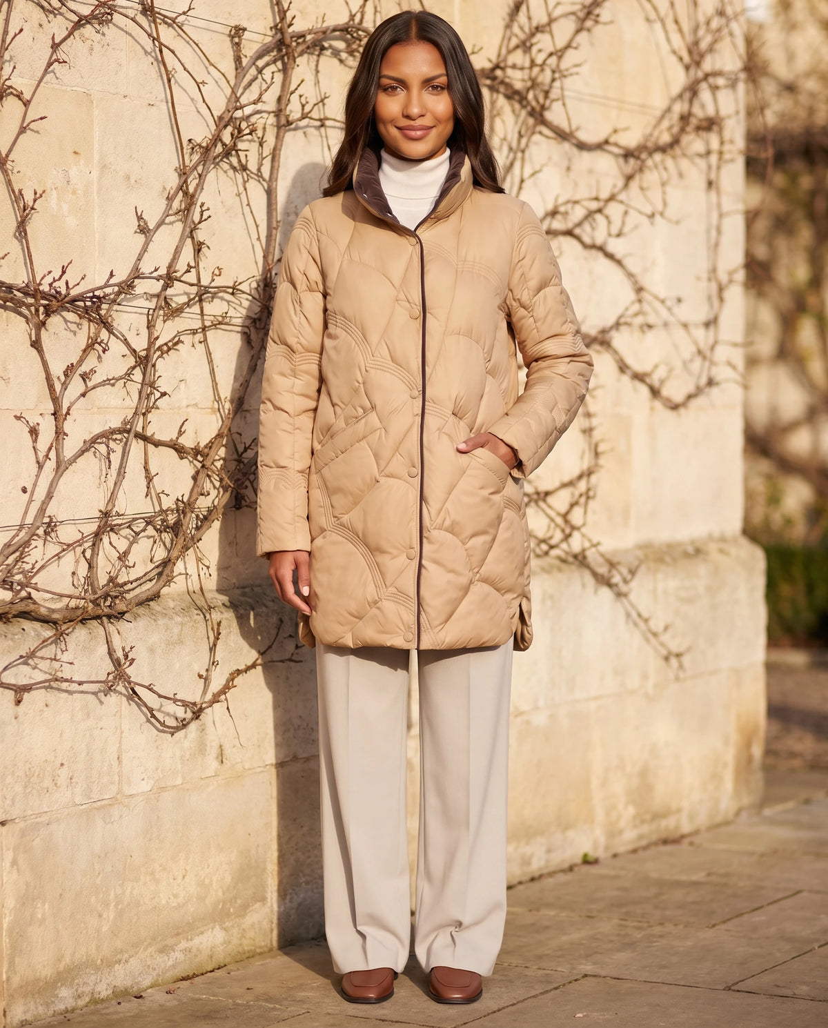 Leichte mittellange Steppjacke mit Wellensteppung Ludmila in Camel, getragen entlang einer hellen Steinmauer