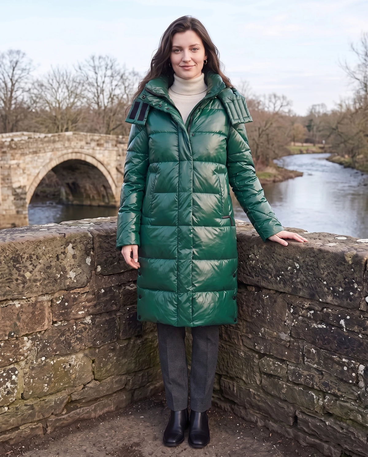 Doudoune longue brillante Elena en Vert Émeraude, portée sur un pont de pierre