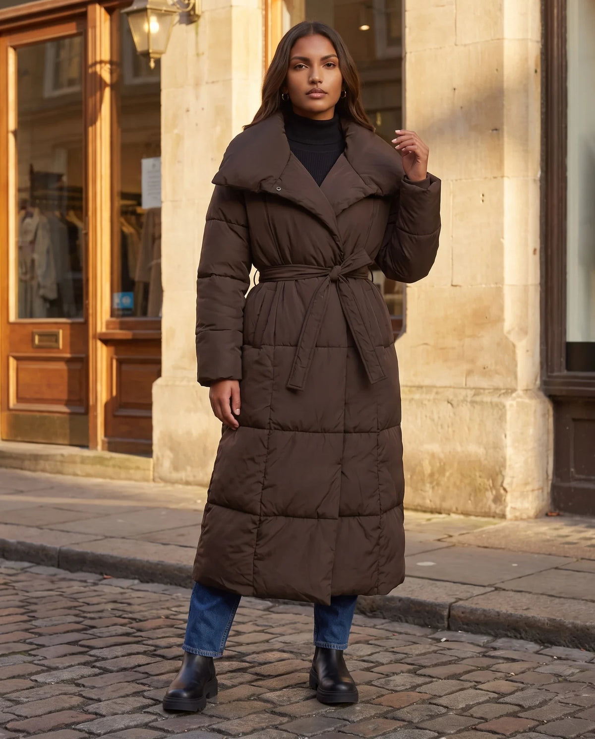 Doudoune longue matelassée Eudeline en Chocolat portée dans une rue pavée