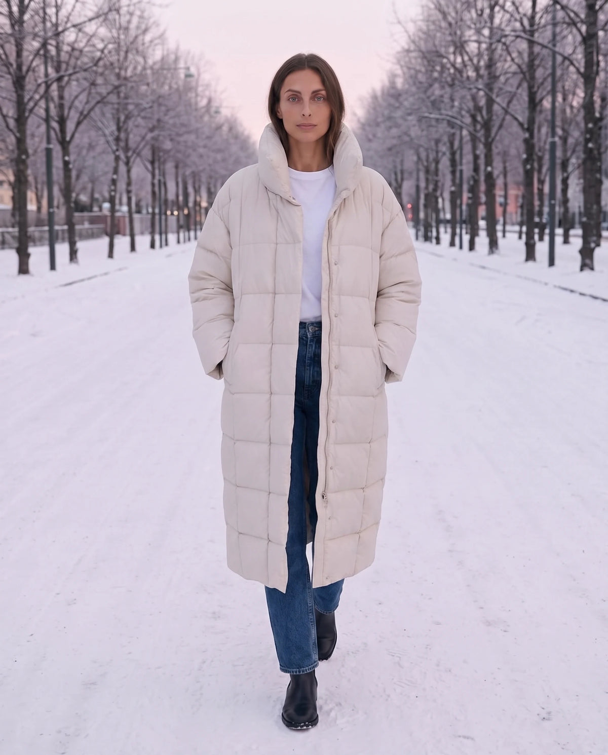 Doudoune longue oversize à col cheminée Laure en Blanc Cassé, portée sur un boulevard enneigé au petit matin, mains dans les poches