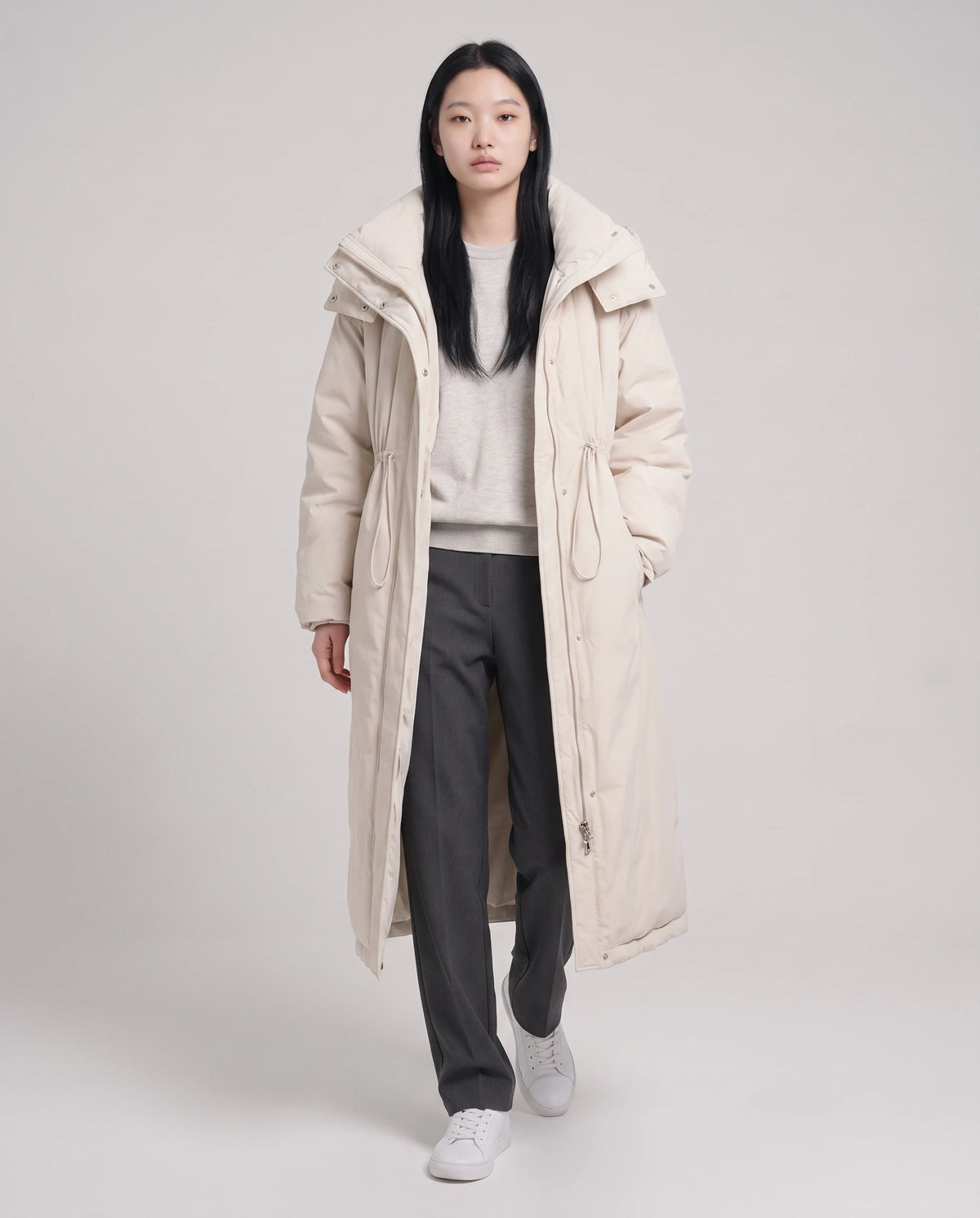 Langer Oversize-Steppmantel mit Stehkragen und Kapuze Lucille in Ecru, offen getragen über graumeliertem Pullover, Kordel gelockert
