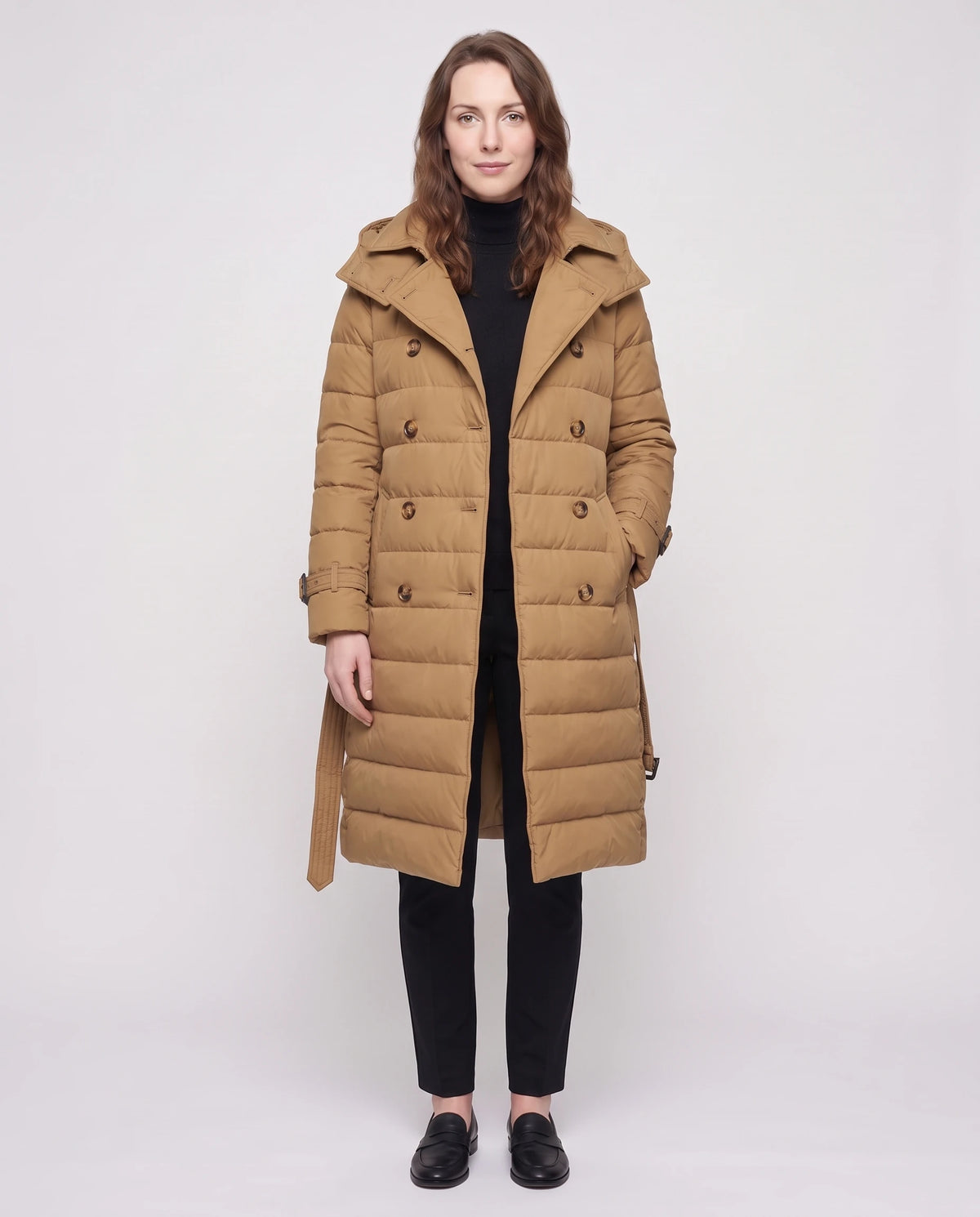 Doudoune longue façon trench à capuche et double boutonnage Rachel en Camel, portée ouverte, boutons défaits et ceinture libre sur un col roulé noir