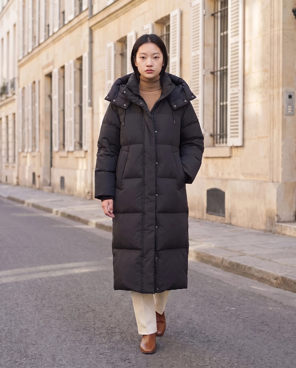 Doudoune maxi oversize à capuche et pressions Marine en Noir, portée dans une rue de pierre blonde