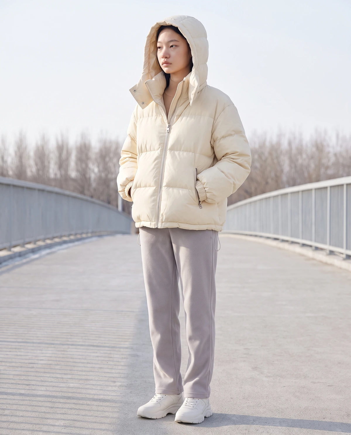 Doudoune courte oversize à capuche amovible Camélia, coloris Blanc Cassé, capuche relevée sur une passerelle en béton