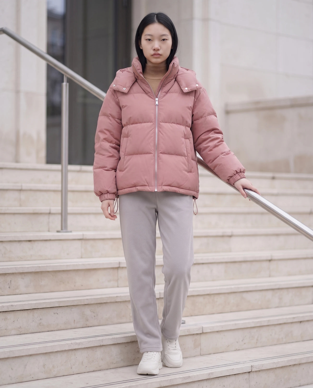 Doudoune courte oversize à capuche amovible Camélia, coloris Vieux Rose, portée sur un escalier en pierre claire