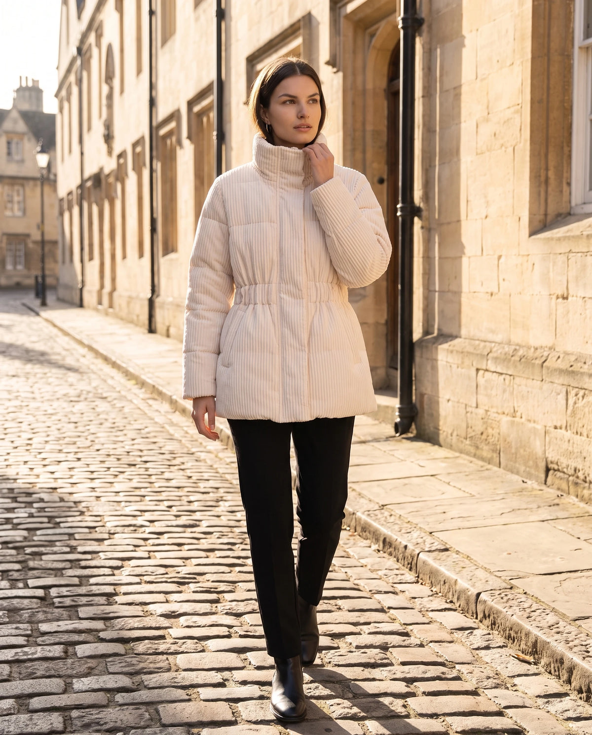 Halblange Plissee-Steppjacke Ilaria in Beige, getragen in einer hellen Steinstrasse