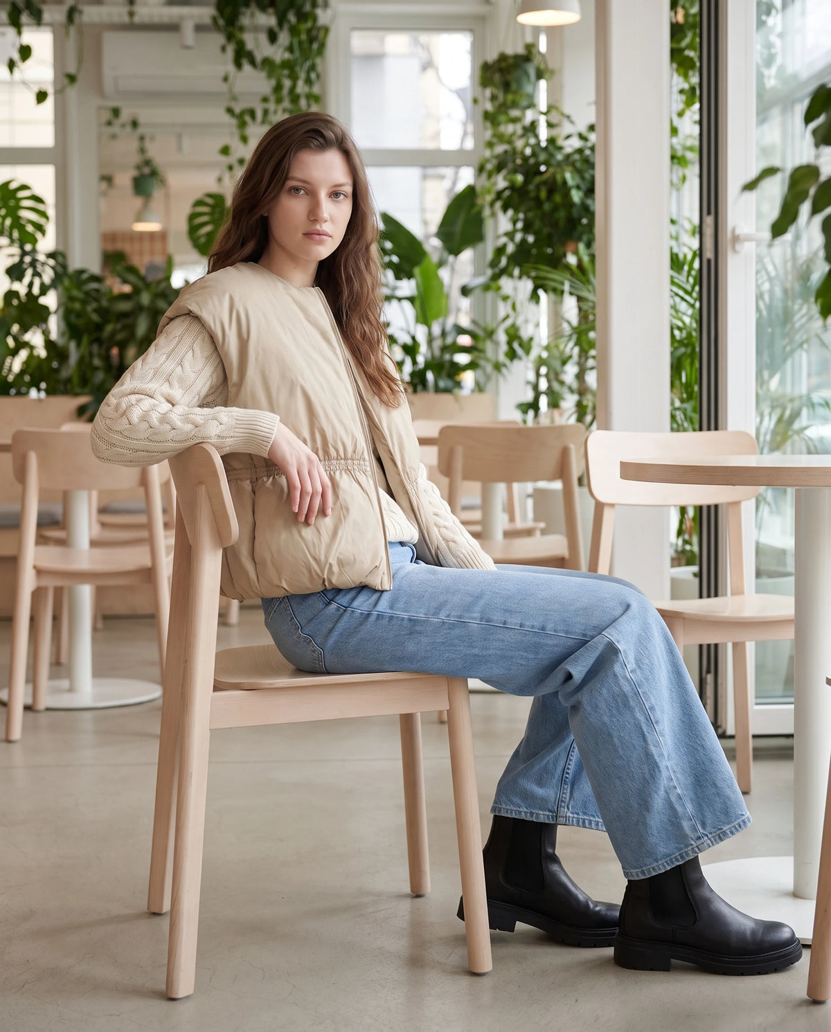 Doudoune sans manches cocon à col rond Béatrix, coloris Lin Naturel, assise dans un café végétalisé