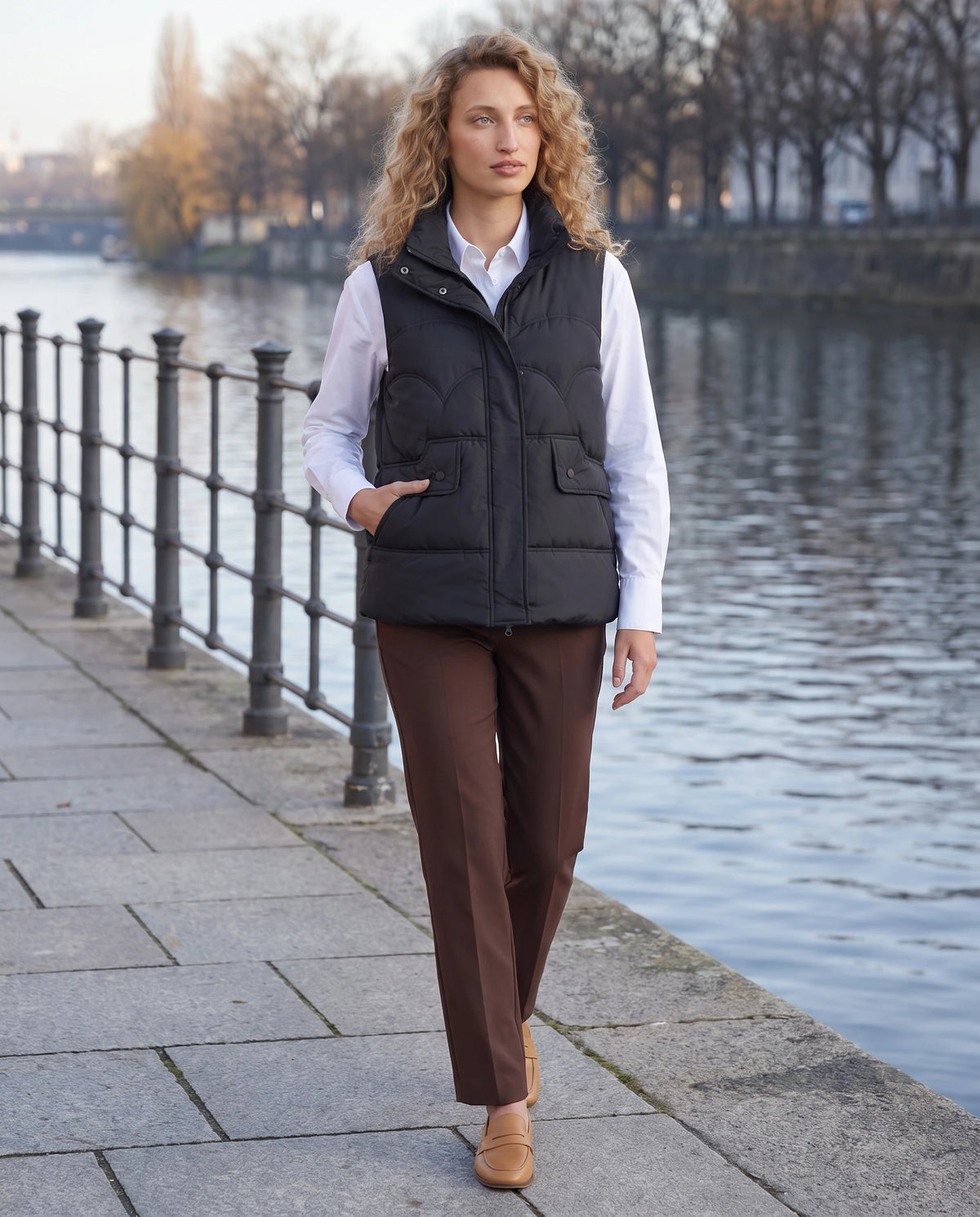 Gilet matelassé court à col montant Sylvie en Noir, porté sur un quai au bord de l’eau