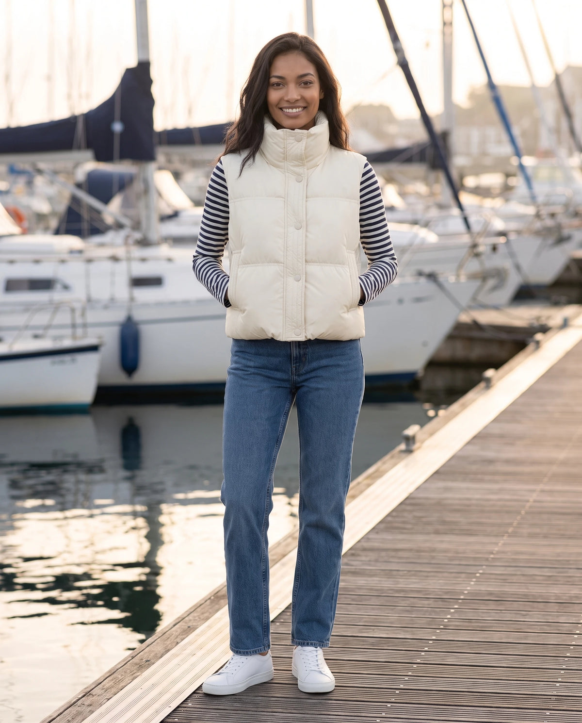 Gilet matelassé cropped à col montant et patte à pressions Soline en Blanc Cassé, portée sur un quai de port aux voiliers amarrés