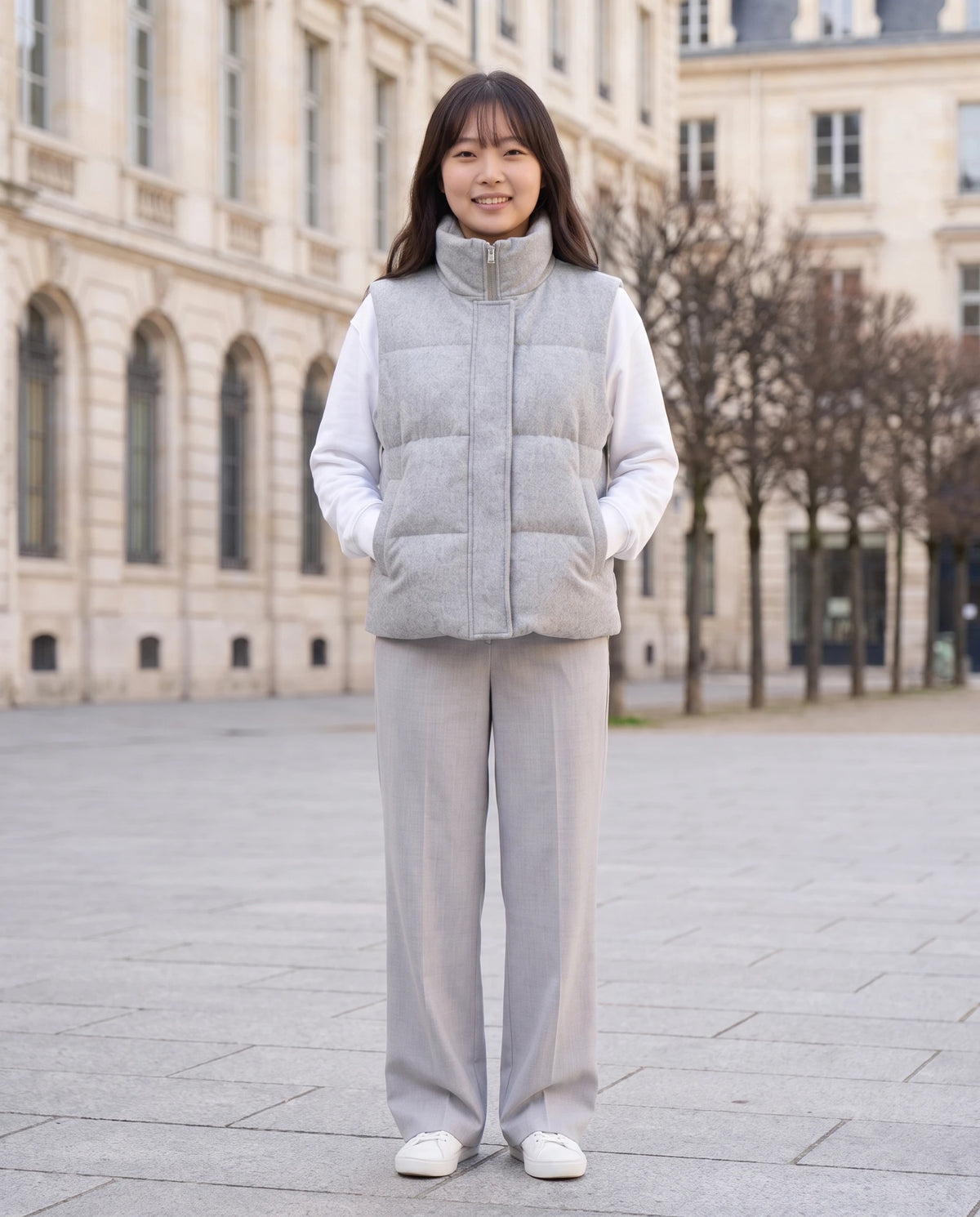Gilet matelassé en lainage chiné à col montant Roxanne en Gris Clair Chiné, portée sur une place de ville aux façades claires