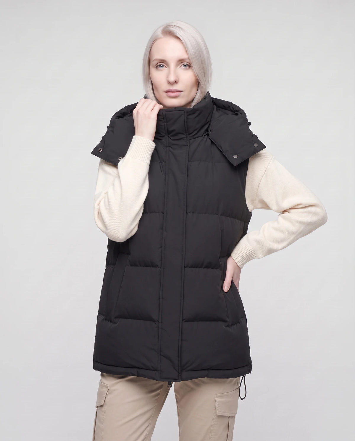 Gilet matelassé oversize à capuche amovible Patricia en Noir, plan rapproché, une main au col, capuche baissée
