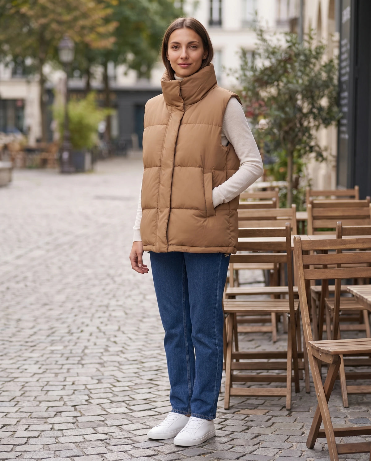 Gilet matelassé oversize à grand col montant et ourlet à cordon Liliane en Camel, portée devant une terrasse de café pavée