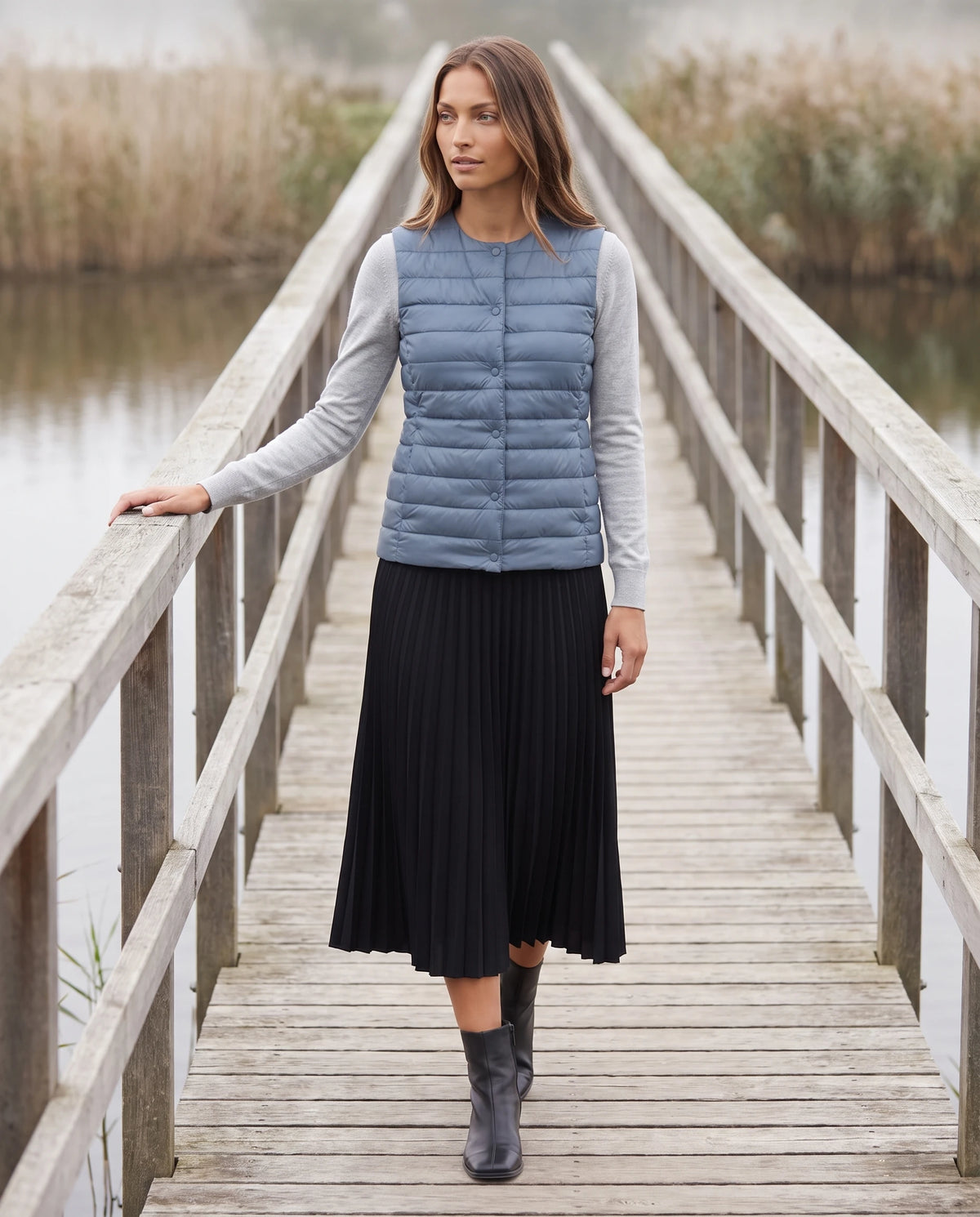 Gilet ultra-léger à col rond transformable Valérie en Bleu Orage, porté sur une passerelle de bois au-dessus de l’eau