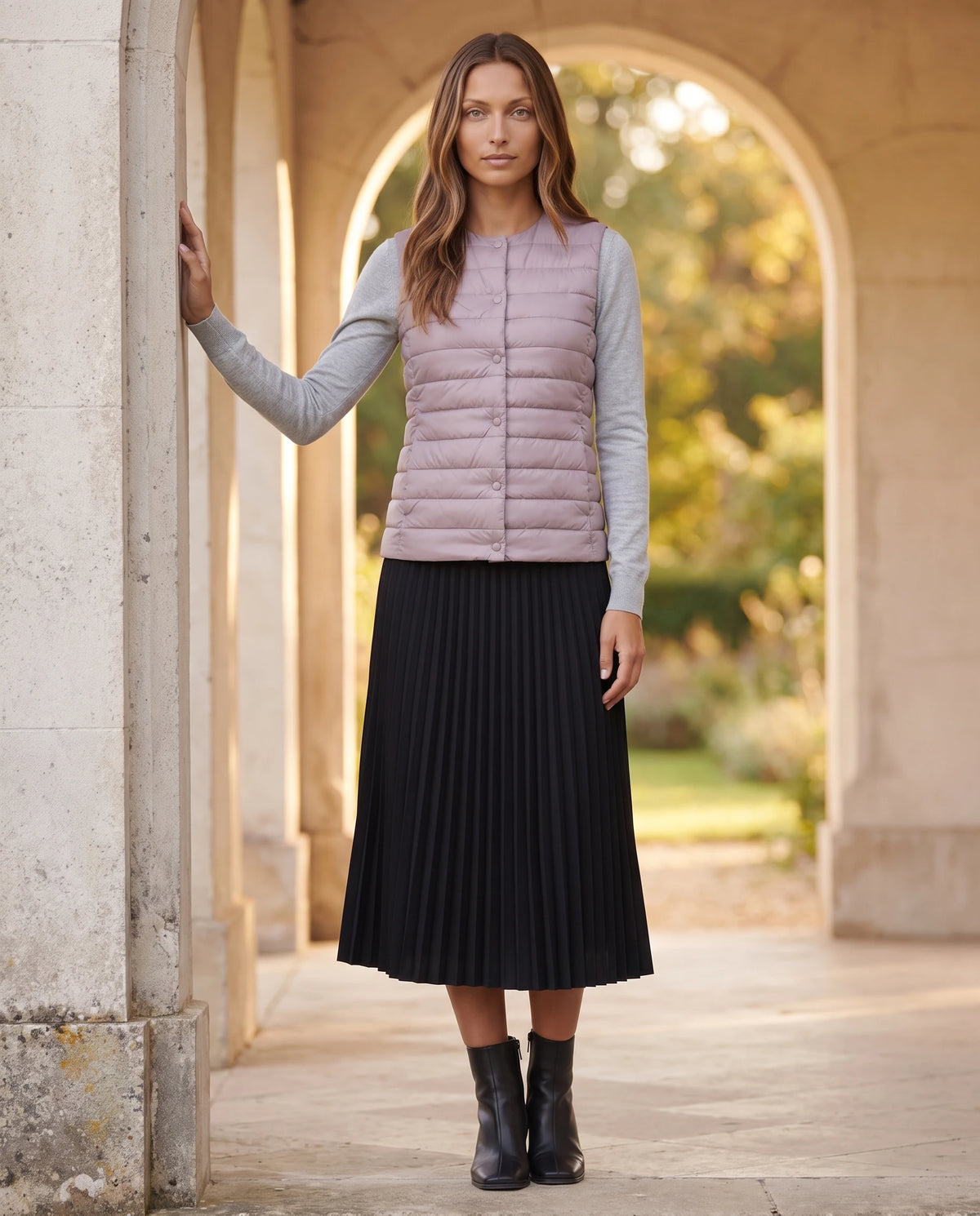 Gilet ultra-léger à col rond transformable Valérie en Mauve Poudré, porté sous une arcade de pierre ouverte sur un jardin