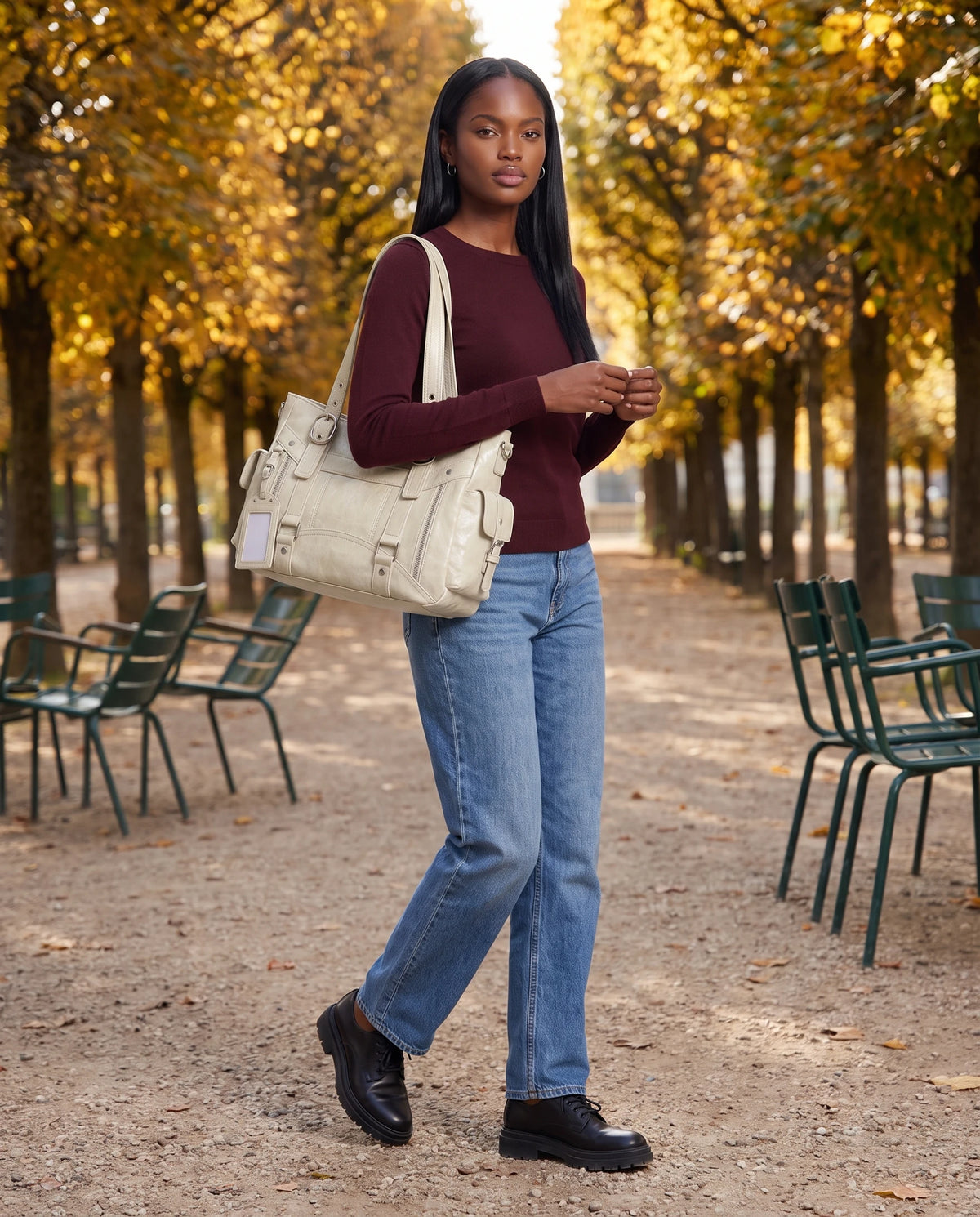 Grand sac à main cabas de cours style motard à boucles Pia coloris Crème, porté à l'épaule dans une allée de jardin public à l'automne