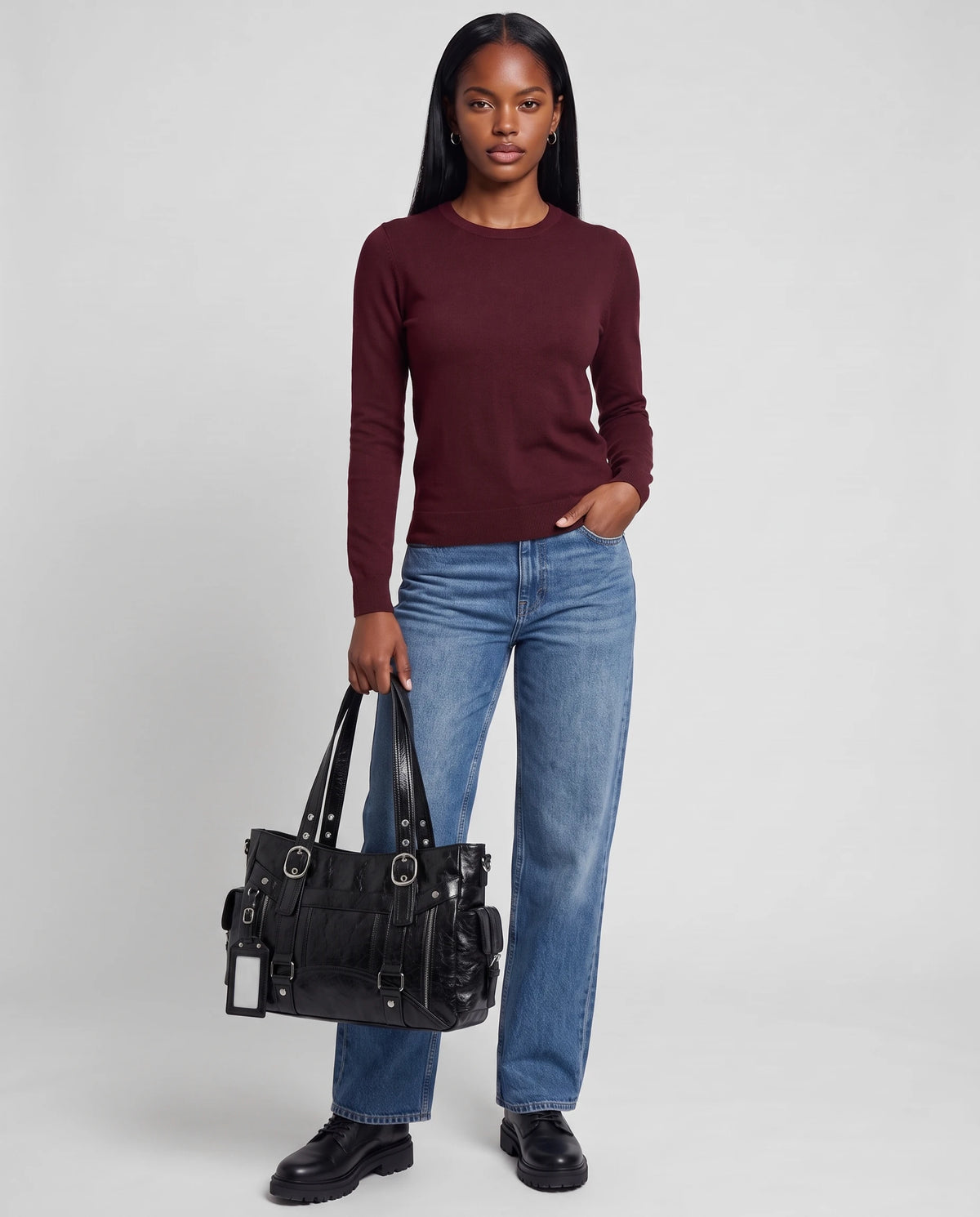 Grand sac à main cabas de cours style motard à boucles Pia coloris Noir, porté à la main par ses deux anses, sur un pull fin bordeaux et un jean droit délavé