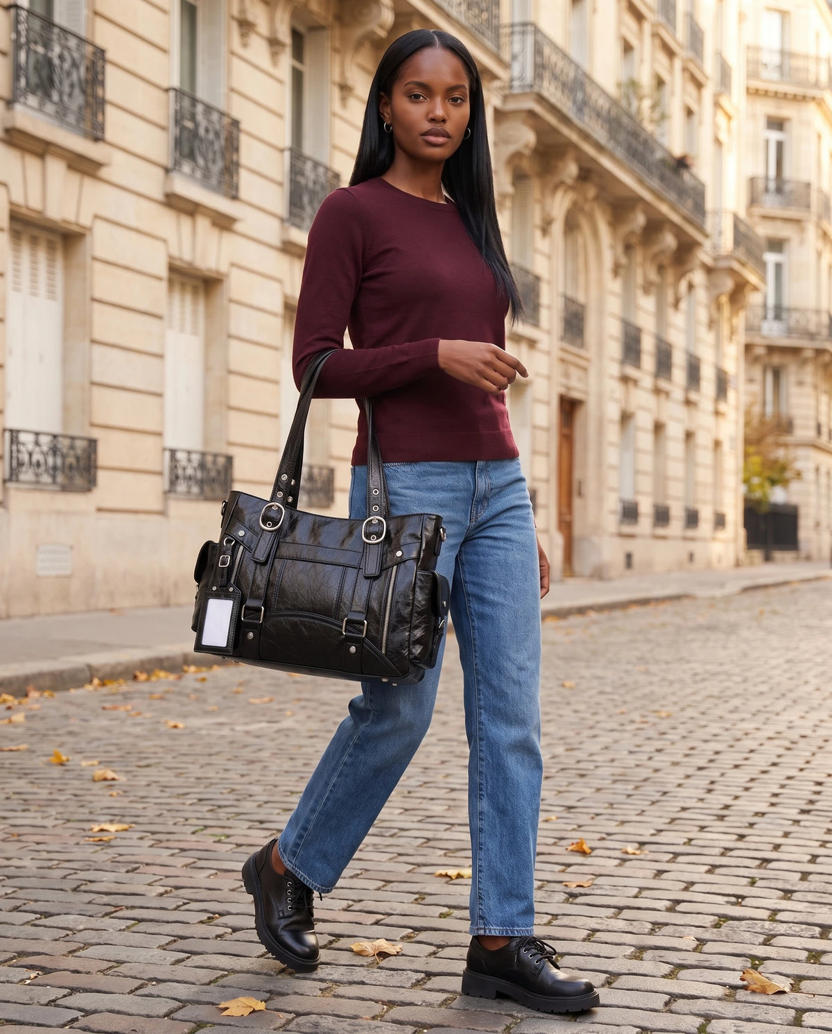Grand sac à main cabas de cours style motard à boucles Pia coloris Noir, porté au creux du coude dans une rue pavée haussmannienne aux feuilles d'automne