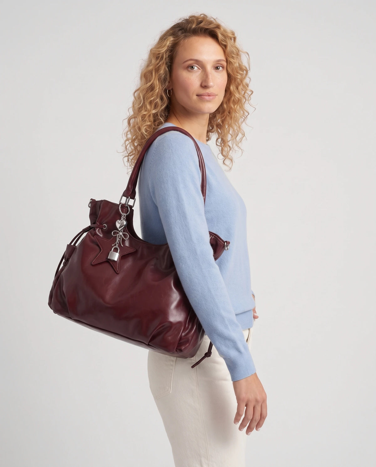 Grand sac à main hobo de cours bandoulière à breloque étoile Lyra coloris Bordeaux, porté à l'épaule par ses anses, calé contre le flanc