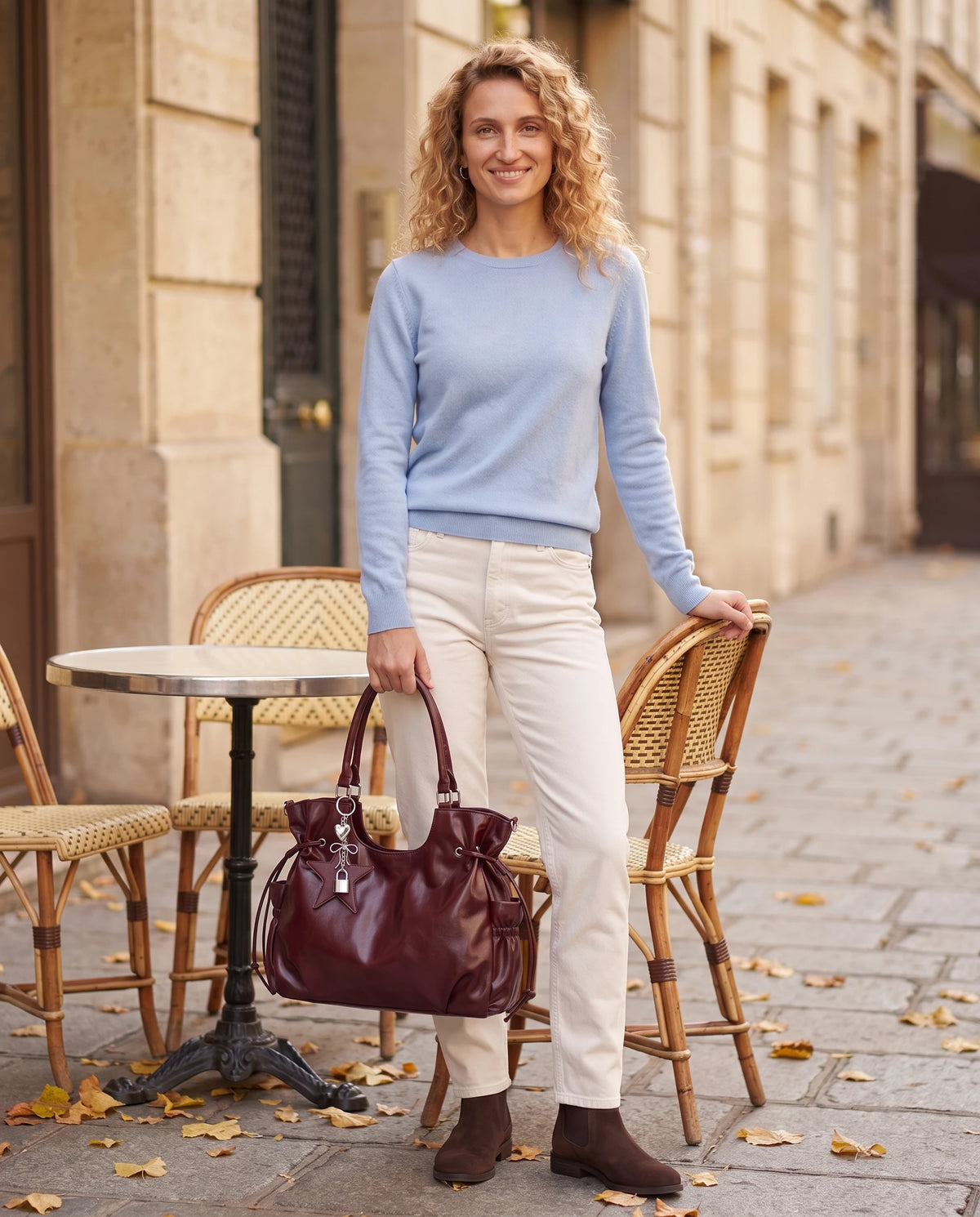 Grand sac à main hobo de cours bandoulière à breloque étoile Lyra coloris Bordeaux, porté à la main sur une terrasse de café parisienne à l'automne