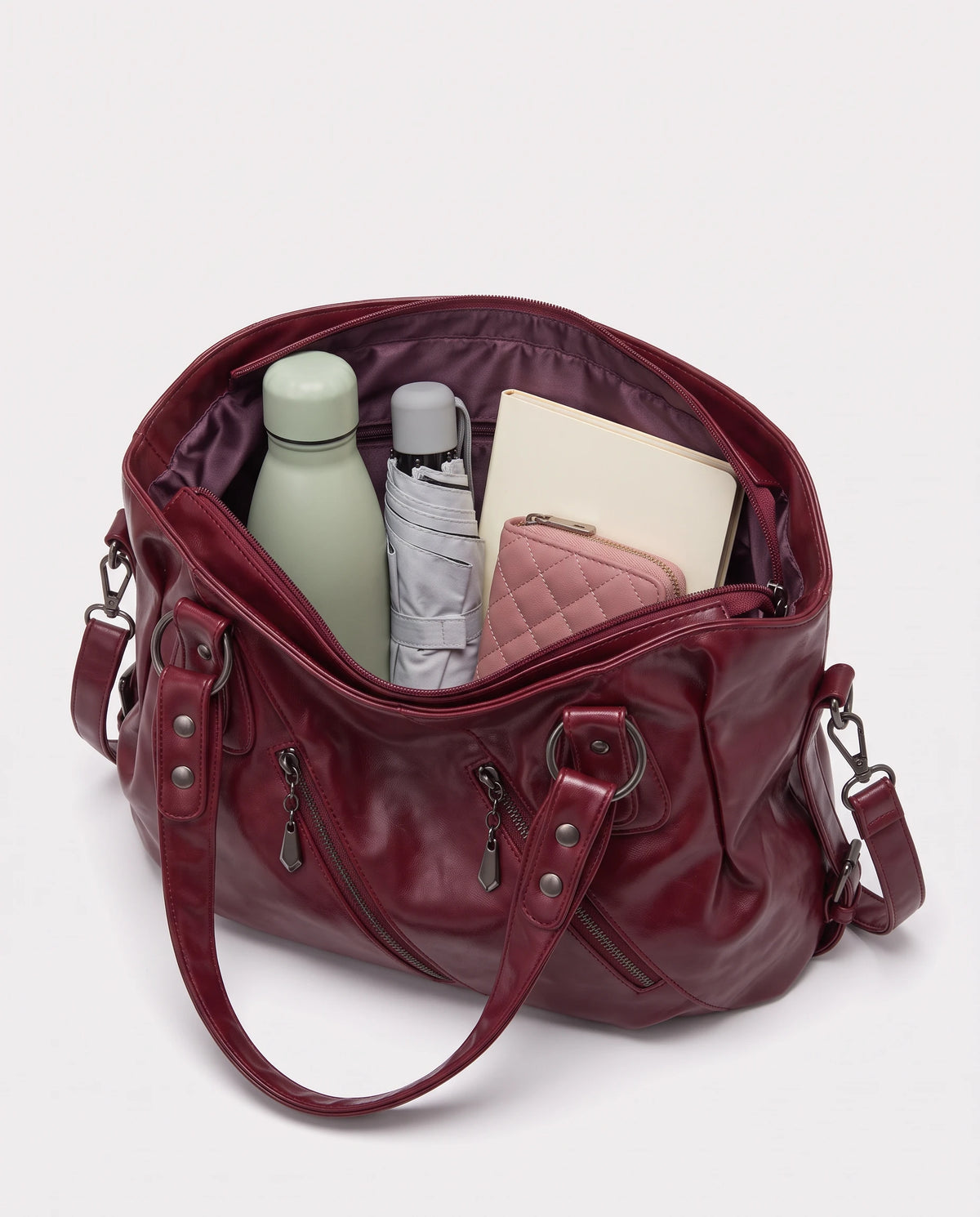Grand sac à main hobo bandoulière style motard à zips Thelma coloris Bordeaux, intérieur rempli d'une gourde, d'un parapluie pliant, d'un portefeuille et d'un carnet