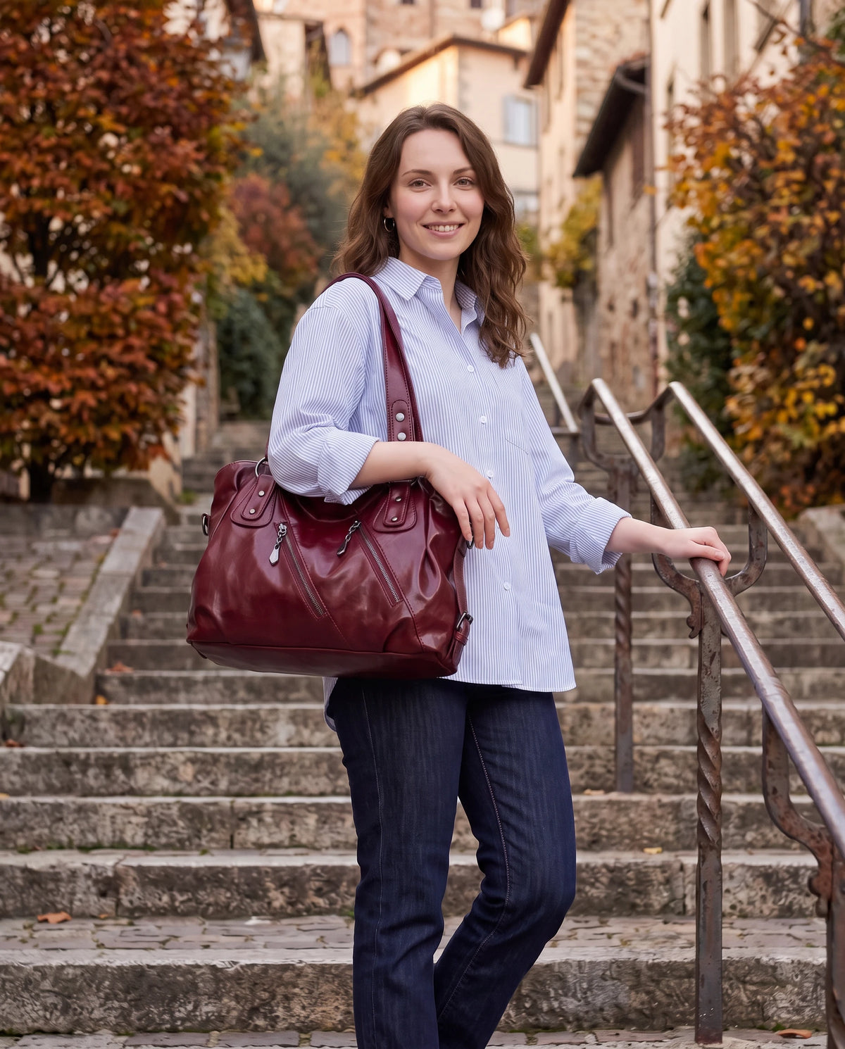 Grand sac à main hobo bandoulière style motard à zips Thelma coloris Bordeaux, porté à l'épaule sur un escalier de pierre en automne