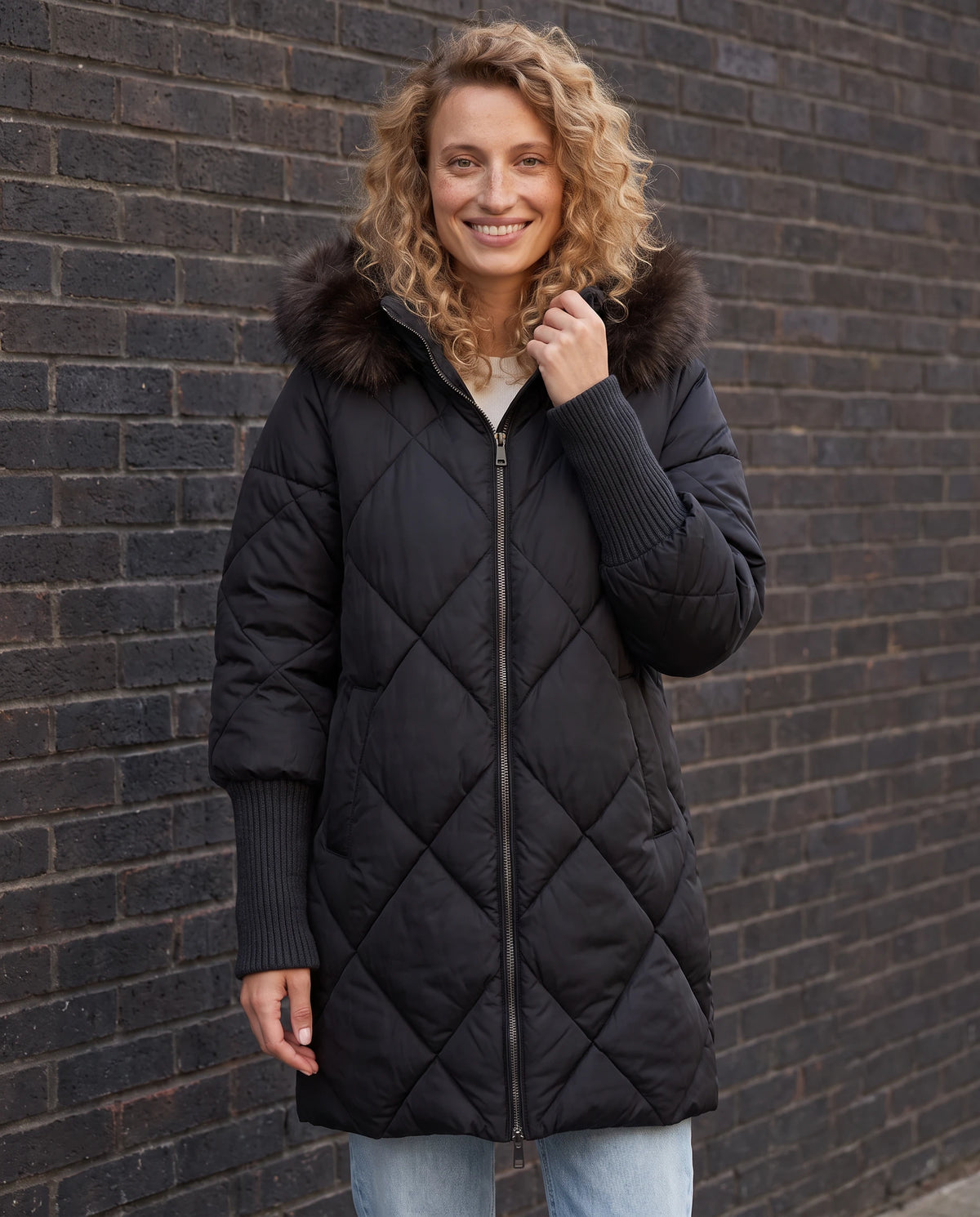 Parka mi-longue matelassée à manches tricot Ava en Noir, portée devant un mur de brique sombre en ville