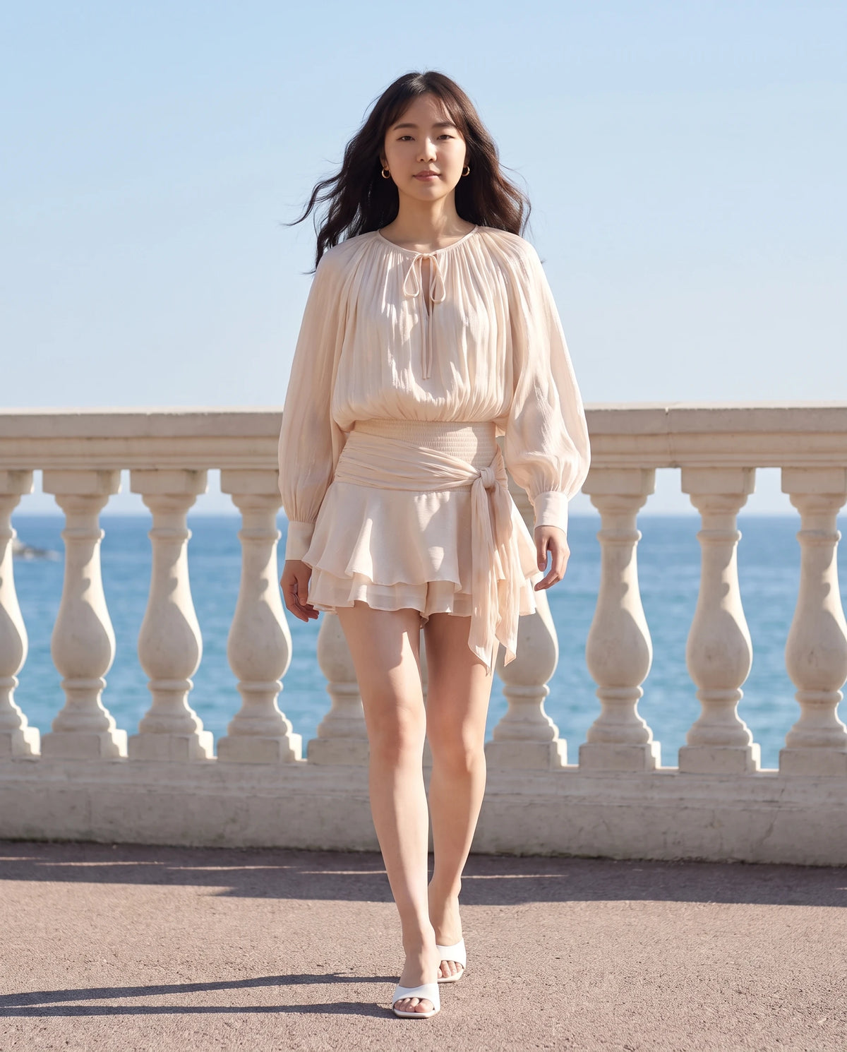 Robe courte tunique en mousseline à manches ballon Louna en Écru, portée sur une promenade de bord de mer