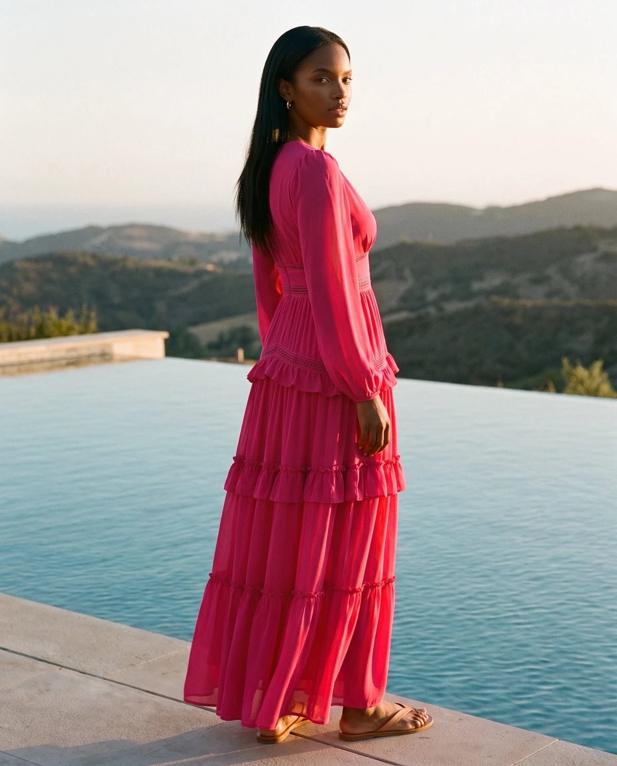 Robe longue bohème à volants et galons crochetés Inaya en Fuchsia, portée au bord d'une piscine au soleil couchant