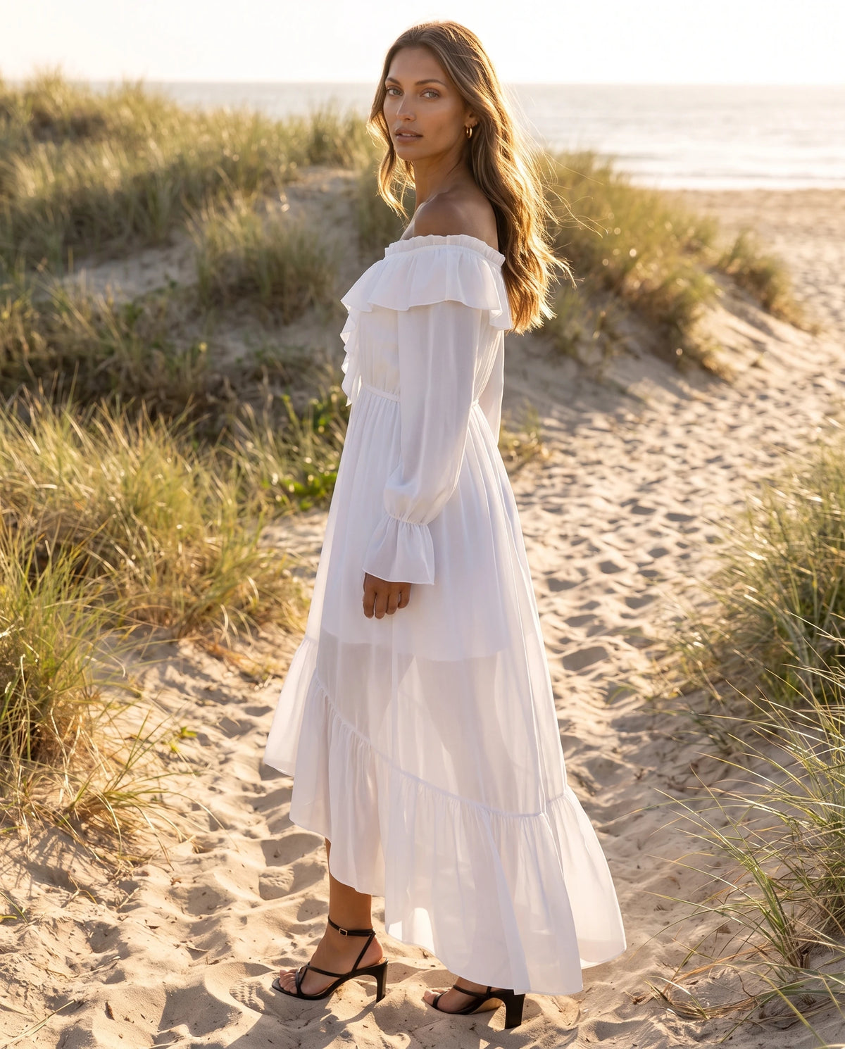 Robe longue en mousseline à col volanté lacé Anaé en Blanc, portée sur un chemin de dunes