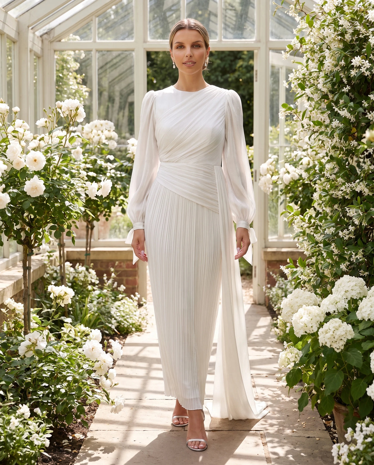 Langes drapiertes Plisseekleid mit Laternenärmeln Élia in Weiß, in einer Orangerie getragen
