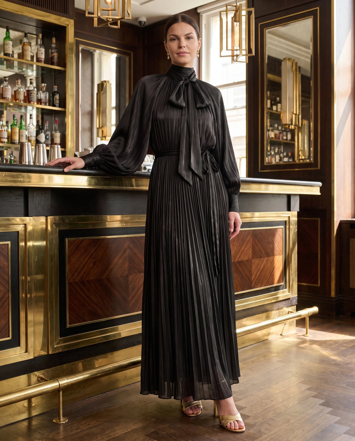 Robe longue plissée à col lavallière et manches chauve-souris Antonia en Noir, portée dans un bar Art Déco