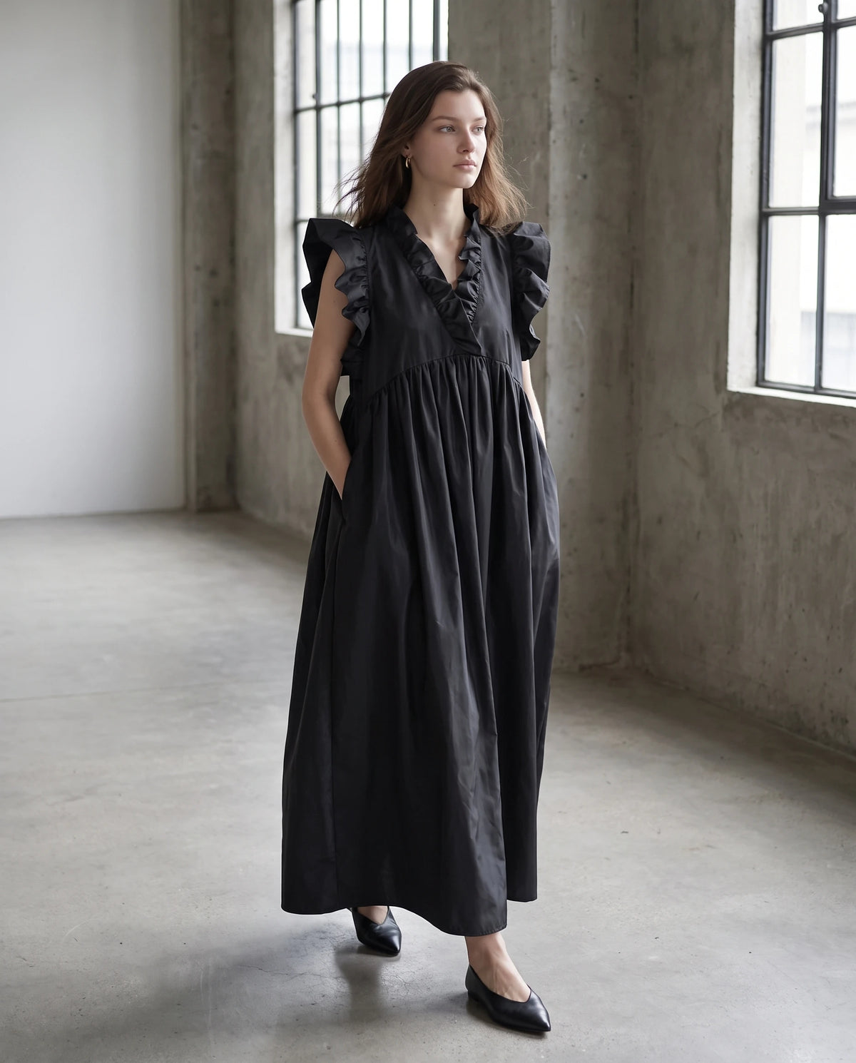 Robe longue ample en taffetas à manches volantées Hermione en Noir, portée dans une galerie de béton brut
