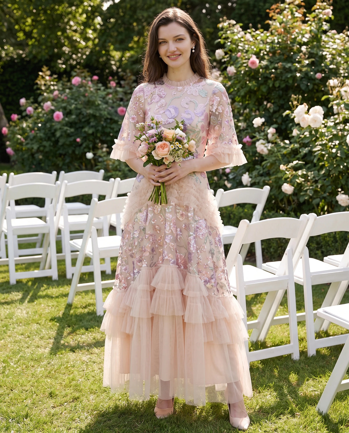Langes Tüllkleid mit Pailletten-Stickerei und Volants Rosalba in Champagner, auf dem Rasen einer Hochzeit getragen
