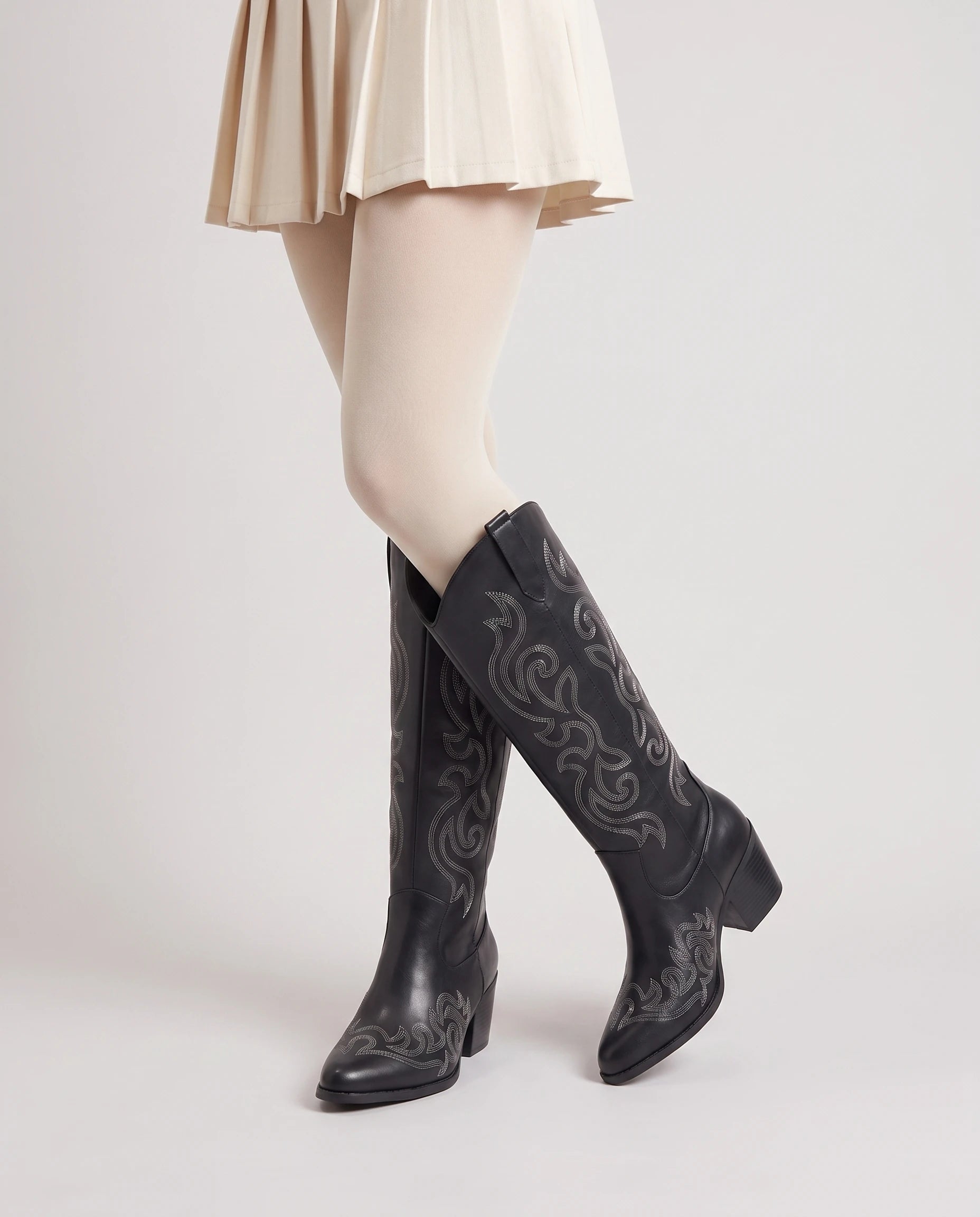 Bottes santiags hautes brodées Ghislaine — Noir, portées en plan rapproché, chevilles croisées