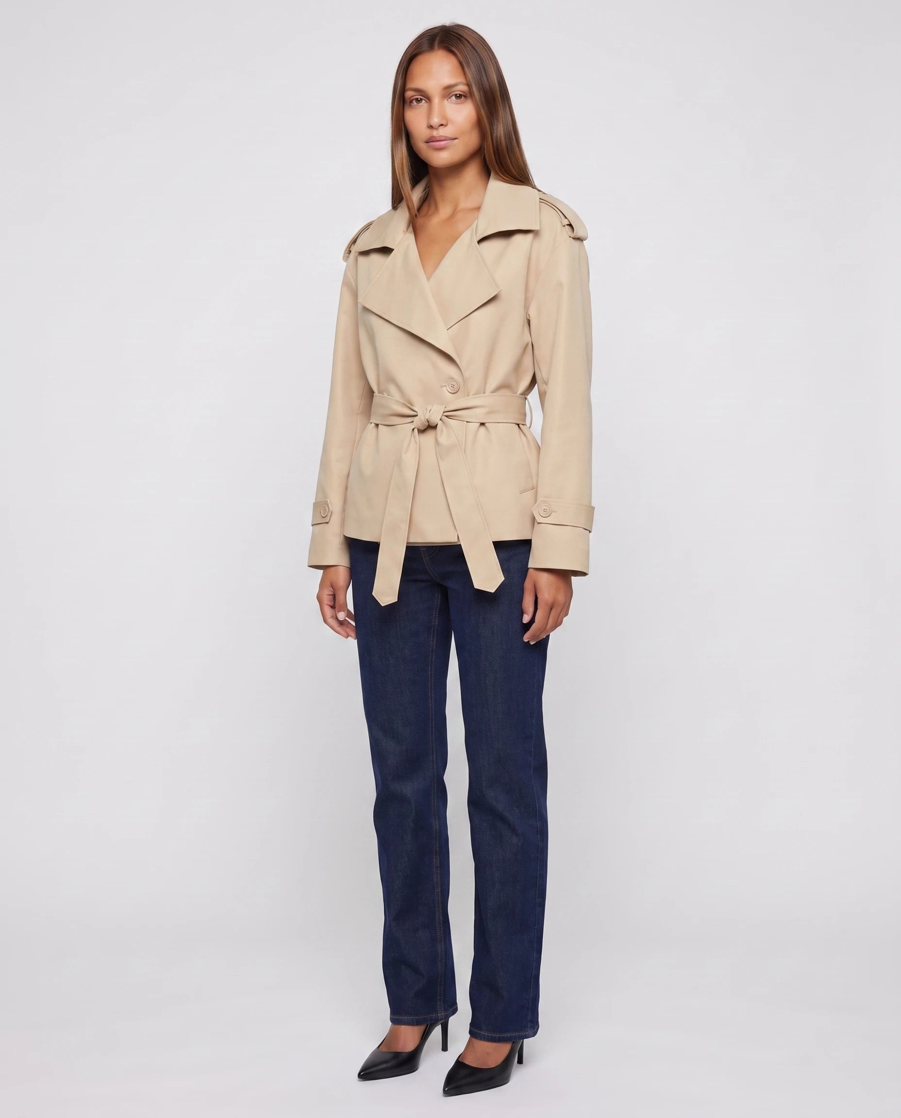 Trench court oversize beige Bettina, main sur la ceinture, vue de face en studio