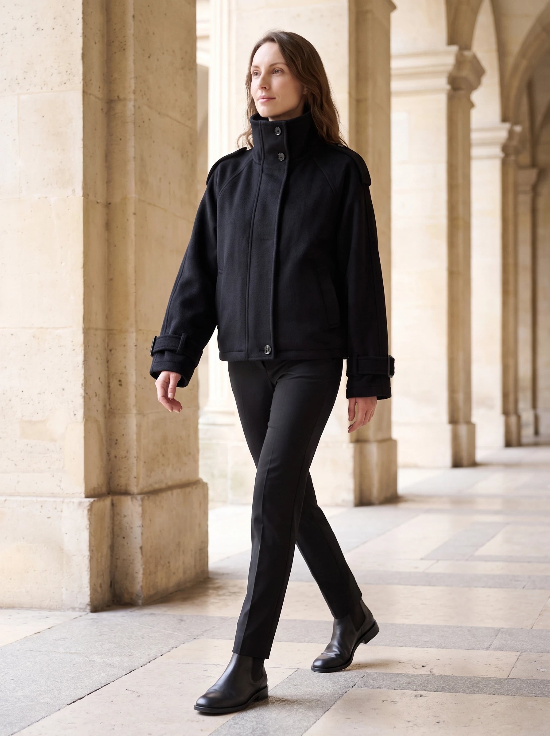 Veste cocon en lainage noir Josiane, portée le long d'une colonnade de pierre