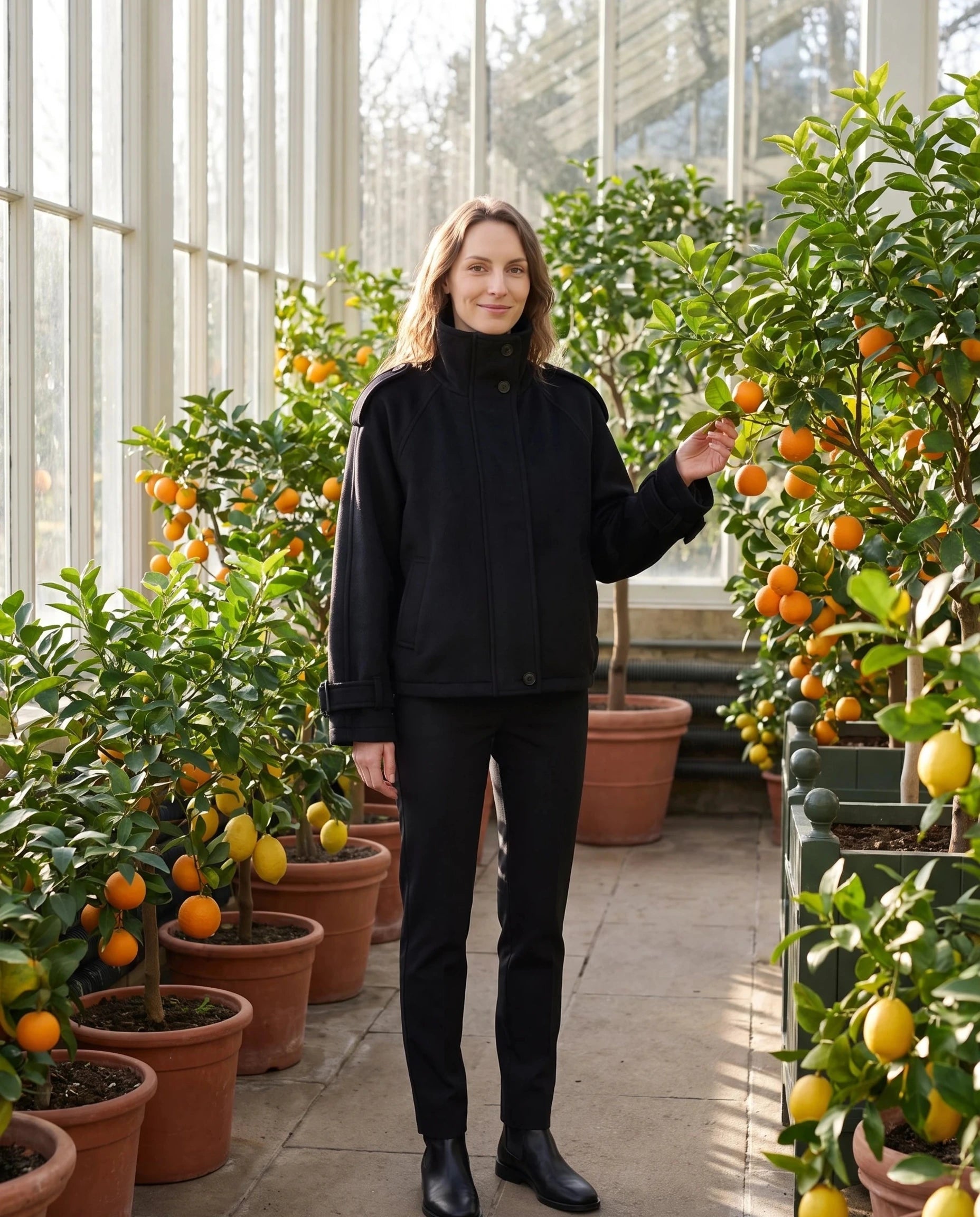 Veste cocon en lainage noir Josiane, portée dans une orangerie aux agrumes
