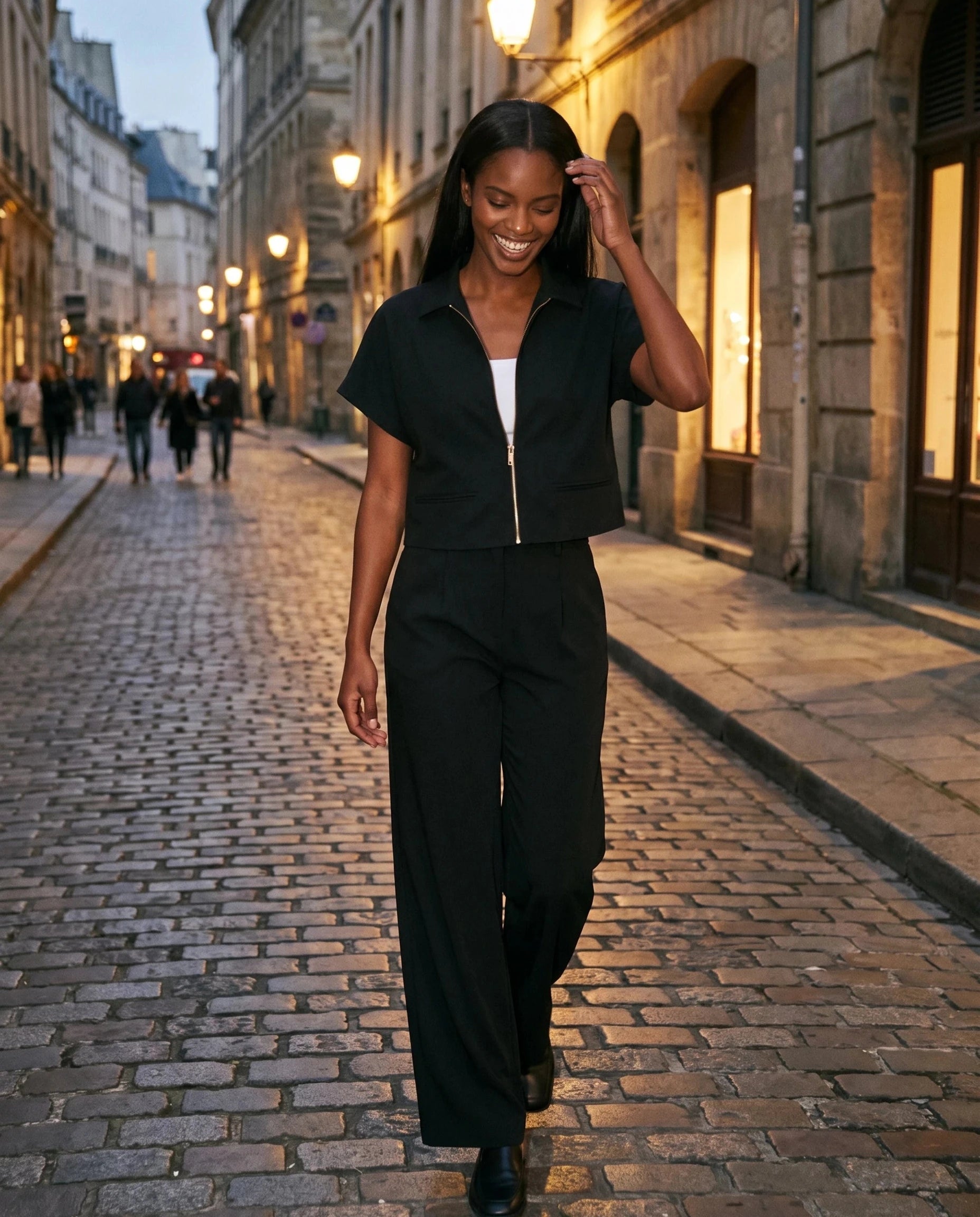 Veste courte zippée noire Gilberte, portée dans une rue pavée au crépuscule