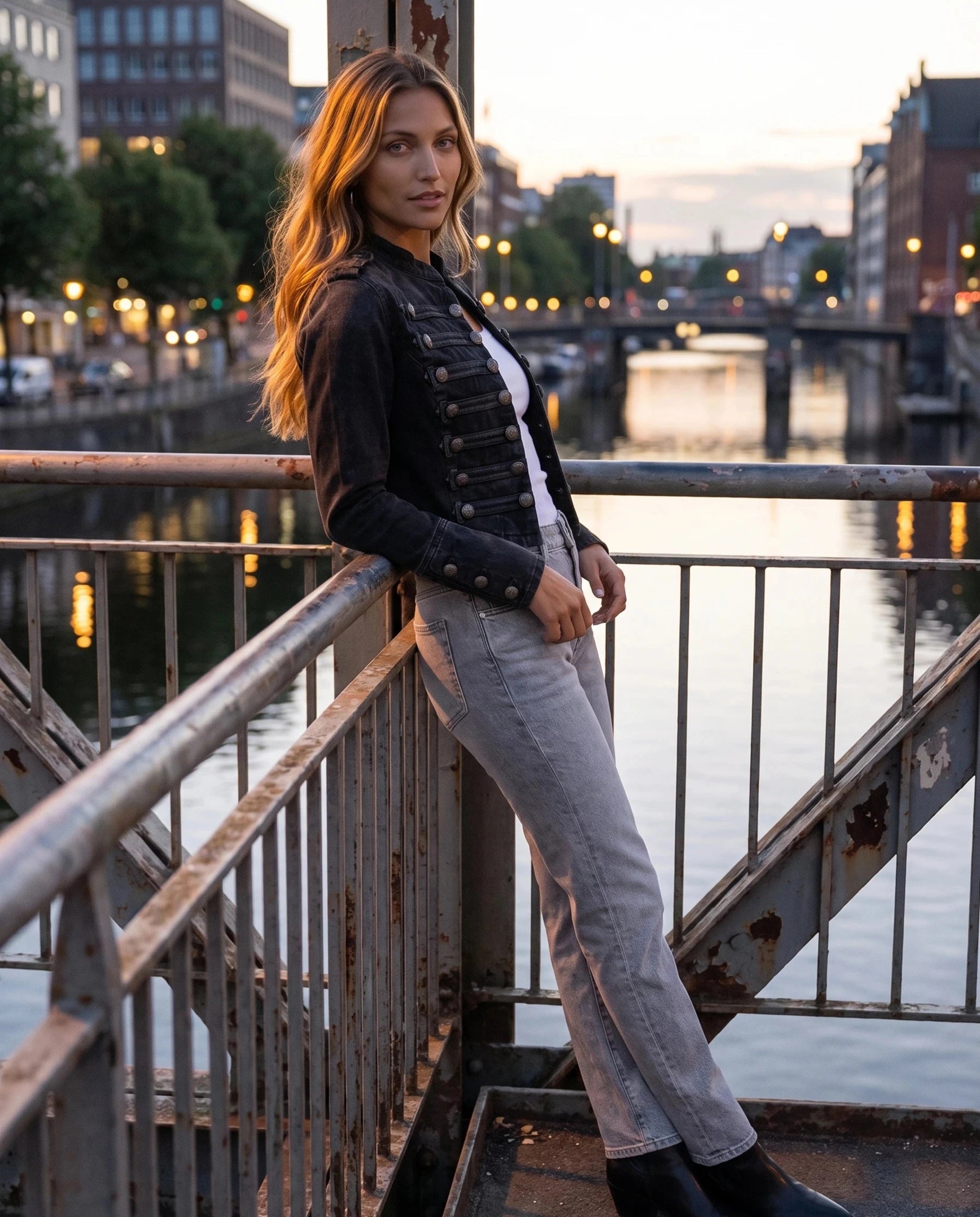 Veste en jean officier noir délavé Rosemonde, portée sur une passerelle au-dessus d'un canal au crépuscule