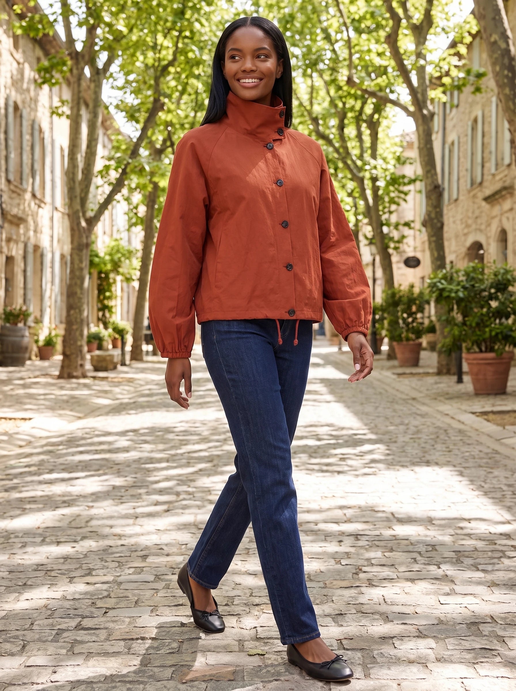 Veste légère rouge Euphrasie, portée dans une allée de tilleuls d'un village